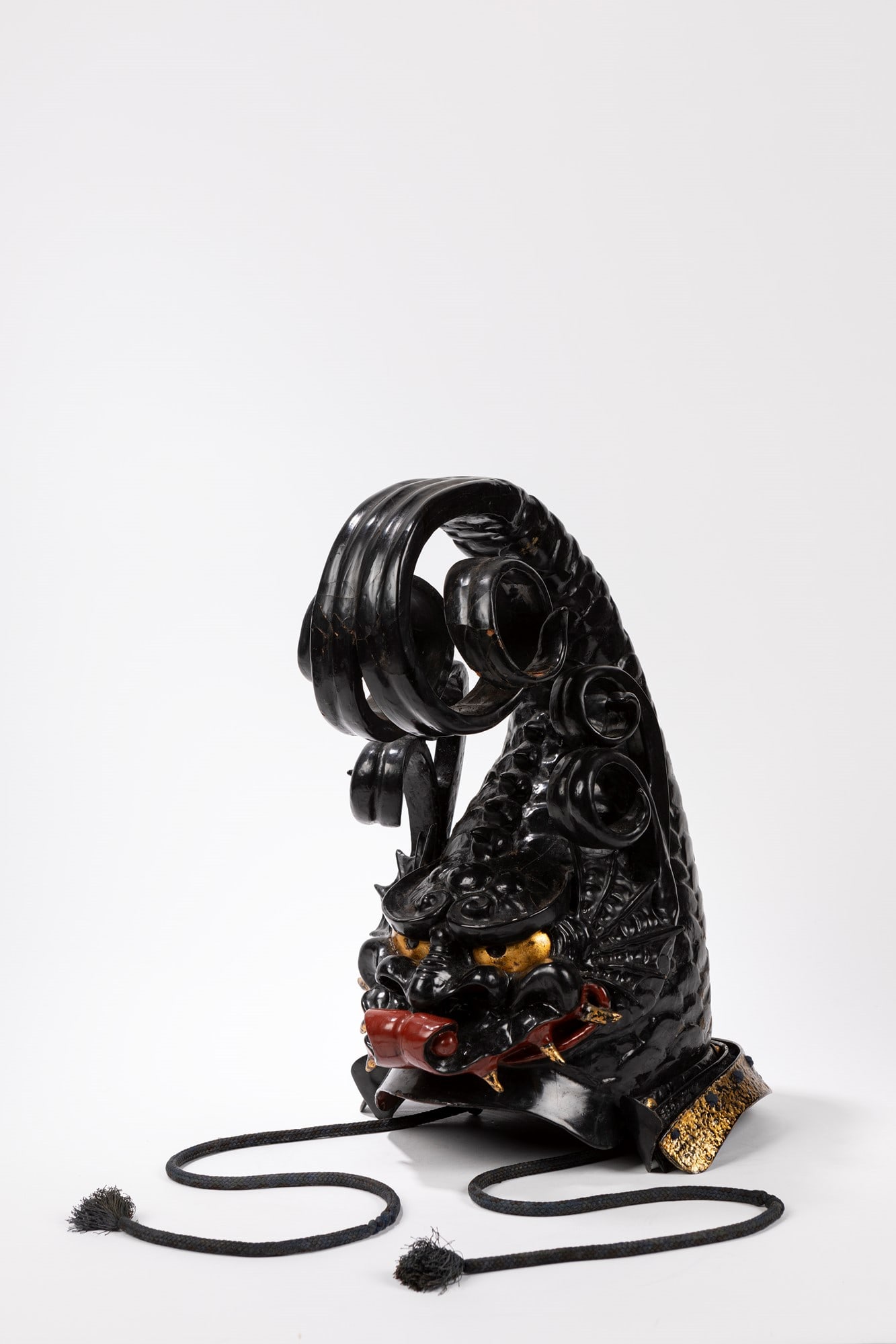 A BLACK AND RED LACQUERED KAWARI KABUTO, Giappone: Representing a fantasy animal with golden eyes and teeth and a spiral terminal; three-bladed shikoro with the last one golden; the inside lined with fabric. Dimensions: h cm 43