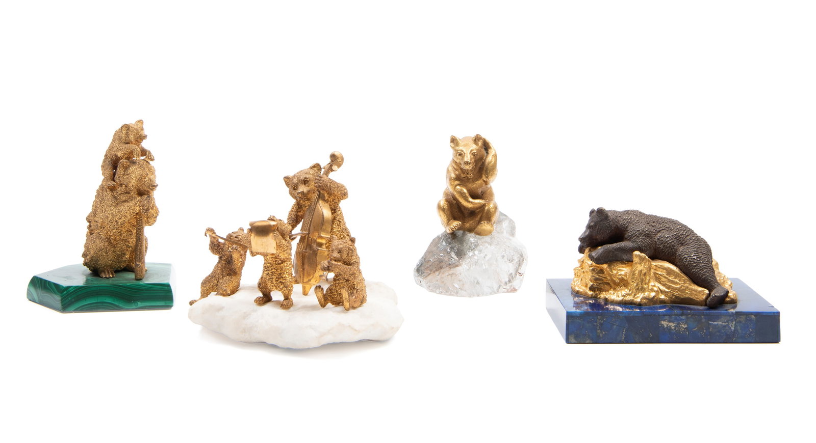 FOUR SCULPTURES IN GILT BRONZE AND HARDSTONES, 20th century: h max cm 9Depicting four bears performing in concert: a recumbent bear on a lapis lazuli base, a bear with a staff and a cub on its back on a malachite base, and a seated bear on quartz.