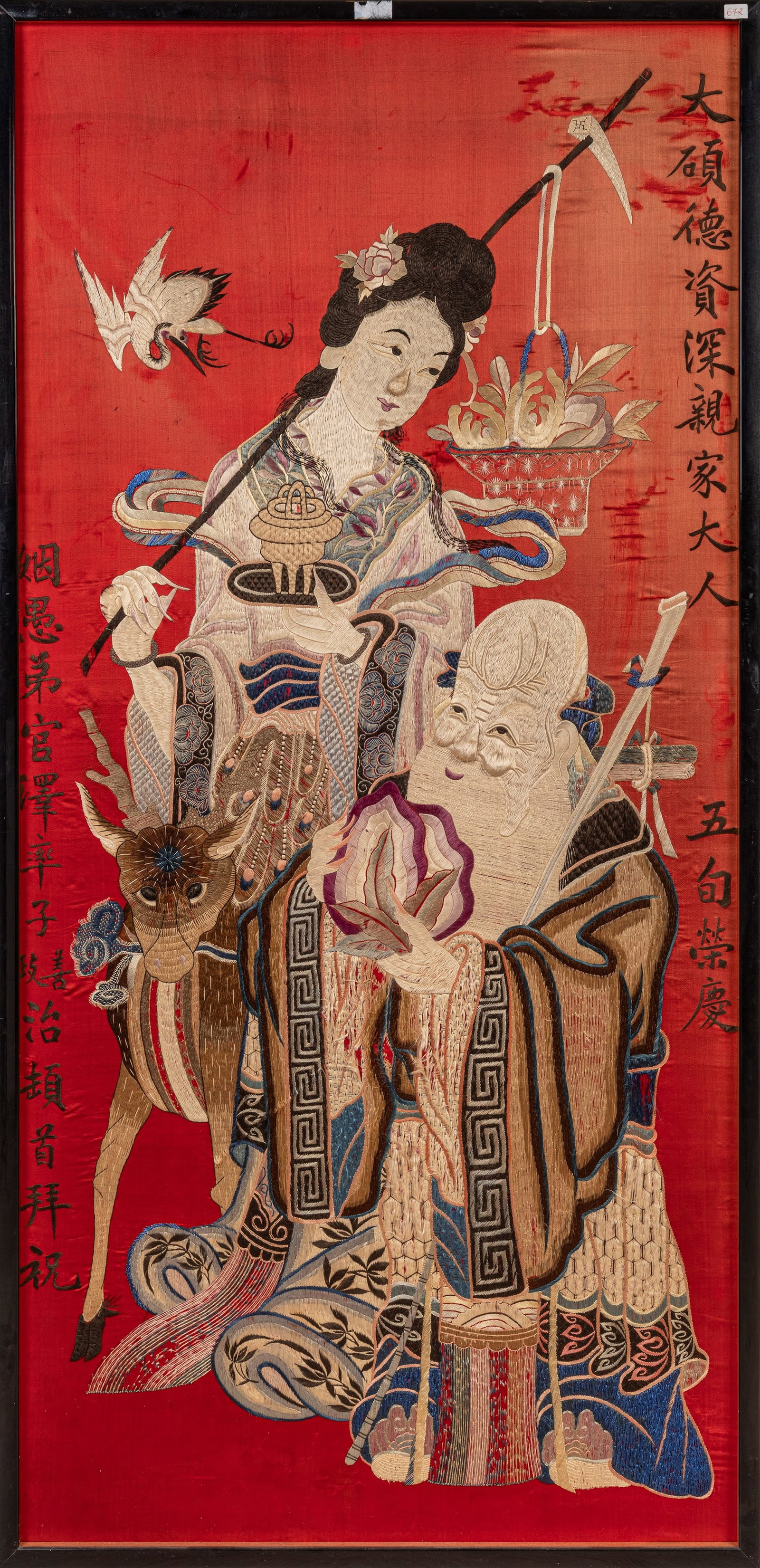 AN EMBROIDERED SILK, China, early 20th century: h cm 144,5 x l cm 68 On a red ground, depicting Shoulao dressed in traditional robes and holding a peach beside He Xiangu shown accompanied by a deer, with a crane in flight in the background. Commemo
