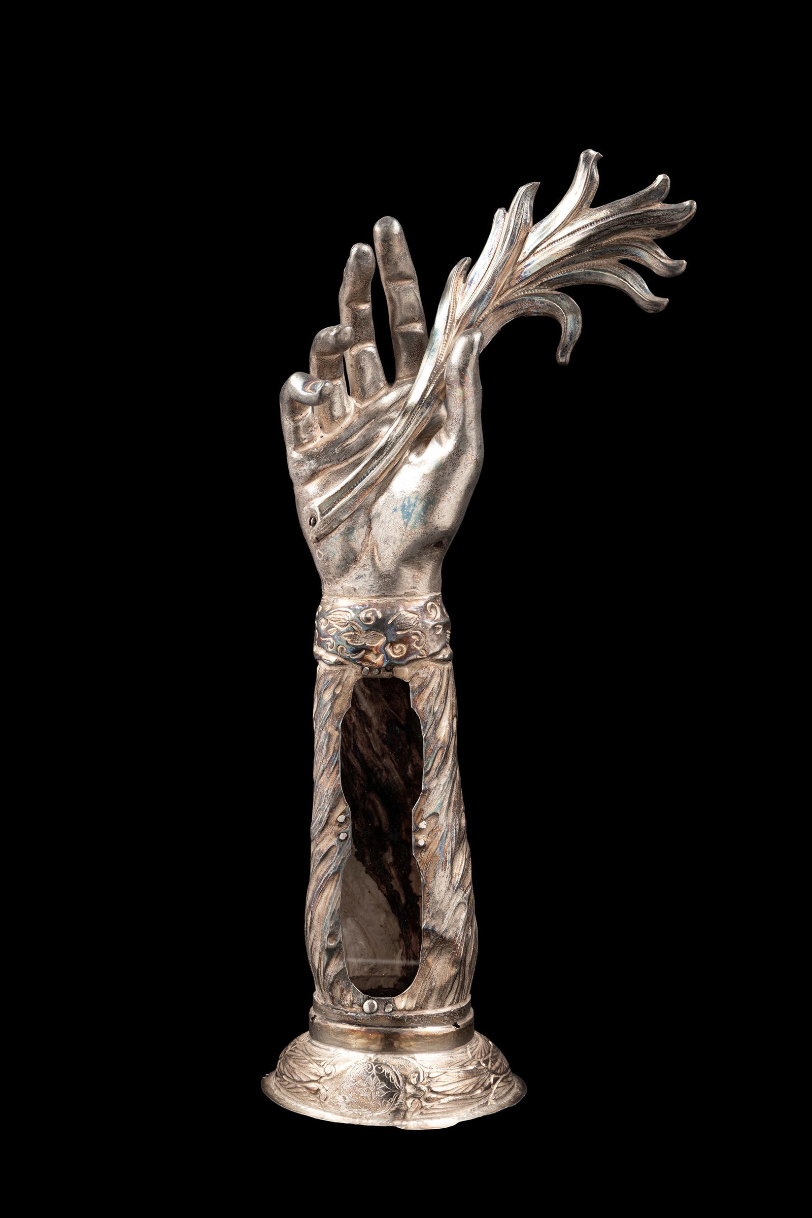 ANTHROPOMORPHIC SILVER RELIQUARY IN THE SHAPE OF AN ARM, Tuscan workshop, 18th century: h cm 36,5.The reliquary consists of an oval base decorated with engraving, featuring a frieze of plant scrolls. In the centre is an oval opening which once contained a relic. The upper part consists o