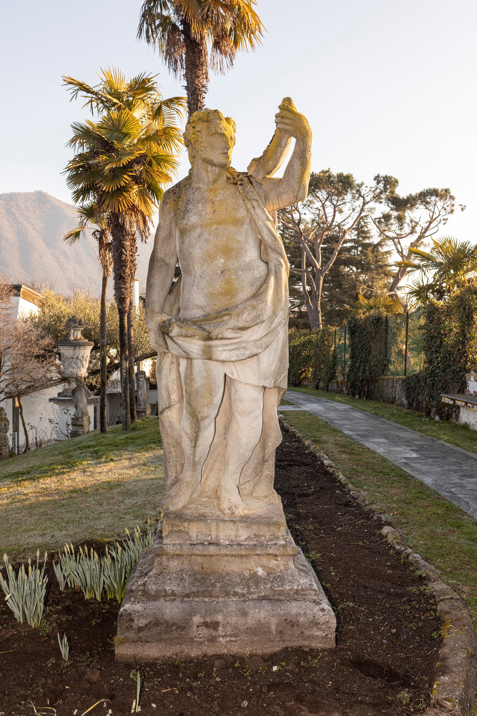 §A LARGE VICENZA STONE SCULPTURE DEPICTING HEPHAESTUS, 19th century: h tot. cm 236 Depicted in a seated position, with a drapery wrapped around the waist, while holding with the left arm the tip of the newly forged spear, in an expressive gesture of triumph (with defec