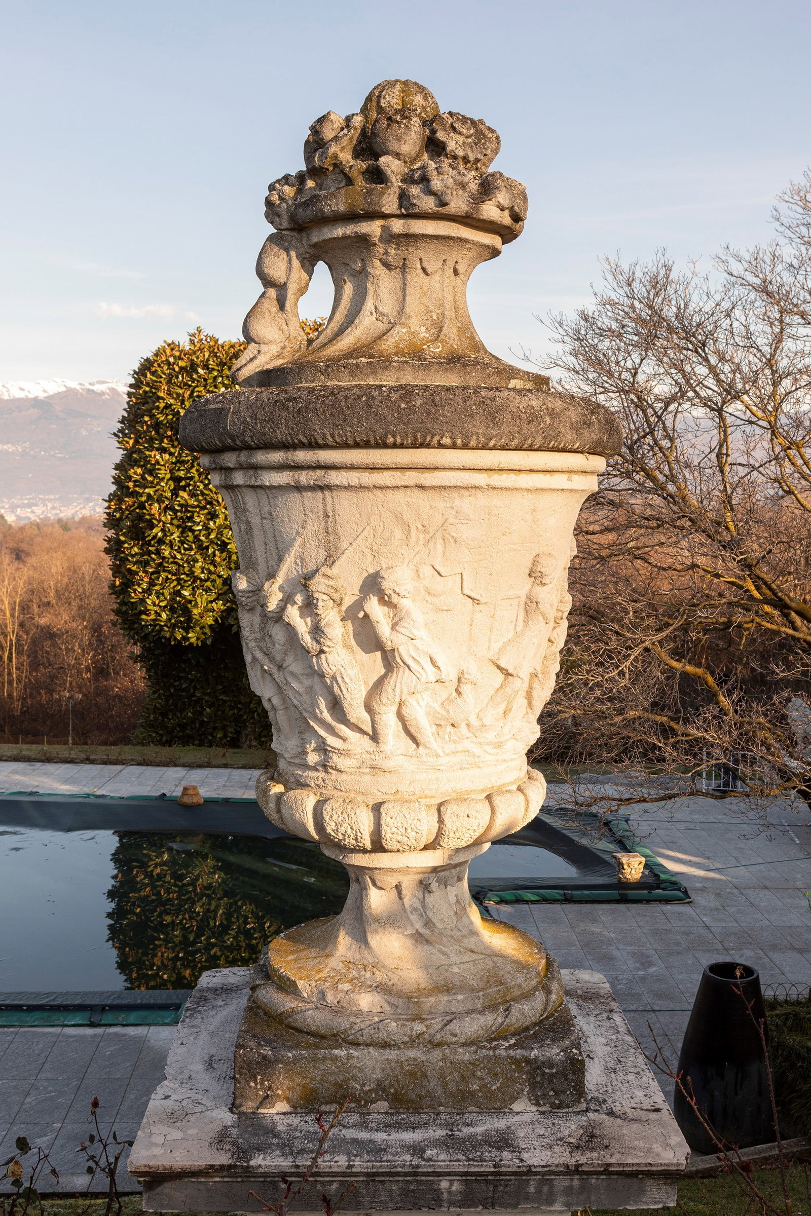 §A LARGE FIGURAL VICENZA STONE VASE WITH LID, Venice, 18th / 19th century: h cm 200 circa It stands on a fluted base; the body is adorned with a refined low relief depicting a procession of figures, among which several gondoliers can be distinguished guiding a boat. The lid 