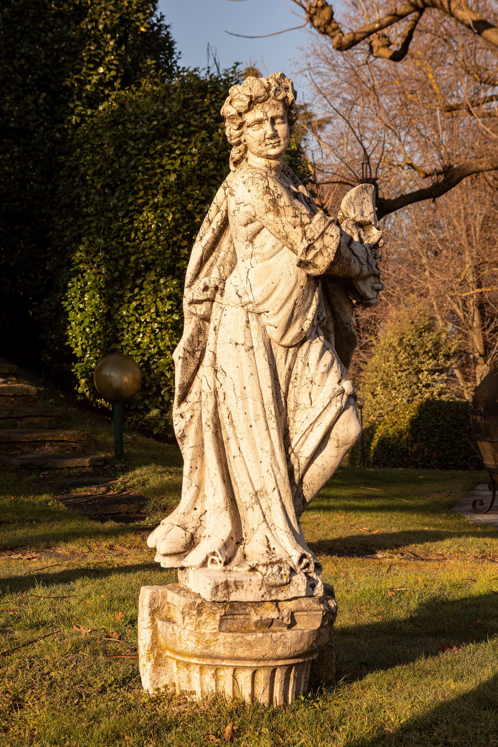 §SCULPTURE IN ISTRIAN STONE DEPICTING THE MUSE MELPOMENE., 17th / 18th century: h cm 120 The figure is depicted standing, draped in rich and heavy folds that enhance its solemnity.The distinctive iconographic element is the large tragic mask held with both hands at the level of t