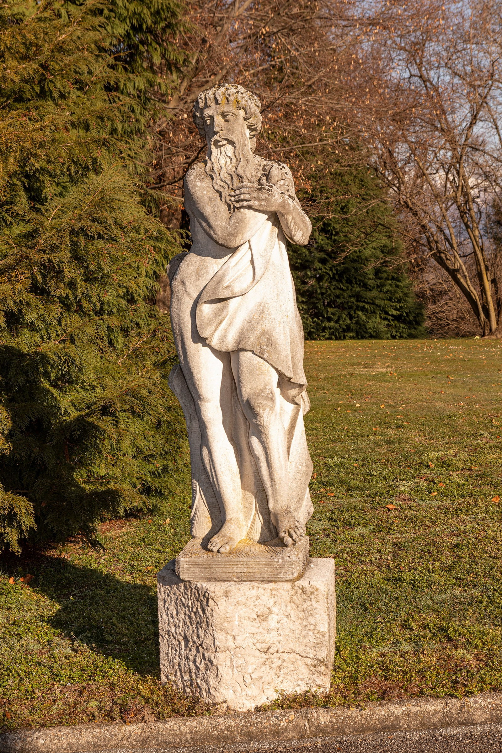 §A VICENZA STONE SCULPTURE DEPICTING SATURN, 19th / 20th century: h tot. cm 210 (base h cm 50) The sculpture depicts a man with a thick flowing beard and curly hair, typical elements in representations of Time or the cold season. The figure is captured in a protecti
