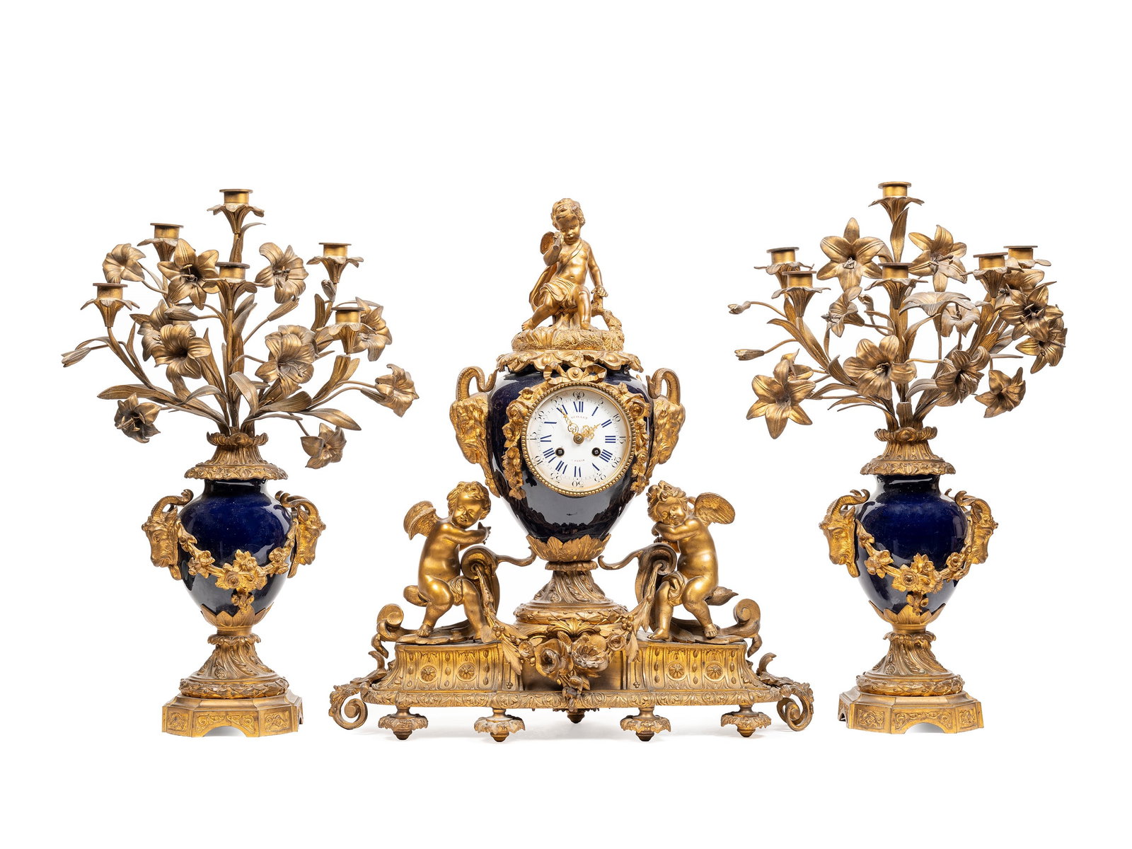 A TRIPTYCH IN PORCELAIN WITH A BLUE GROUND MOUNTED IN GILT BRONZE, France, 19th century: The largest h cm 59 x w cm 50 Composed of a mantel clock decorated with putti, festoons and with two handles in the shape of a roe deer; movement with Roman numerals signed Guillet in Paris; accompani