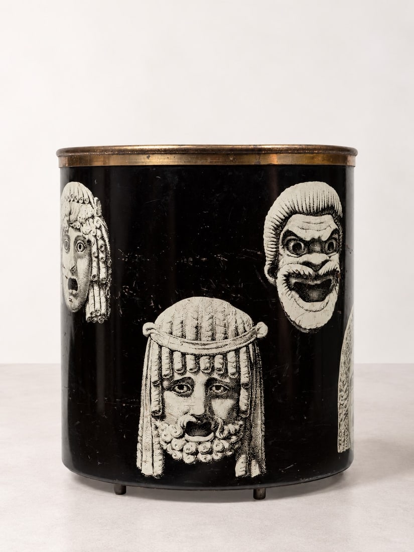 Piero Fornasetti (Milano 1913 - 1988), WASTEPAPER BIN, circa 1960s.: h cm 27,5 x d cm 24 Black lacquered metal, screen-printed with the "Maschere" series decoration, brass rim. Fornasetti production, Milan.Catalogue notes:For the same decoration, applied to a different