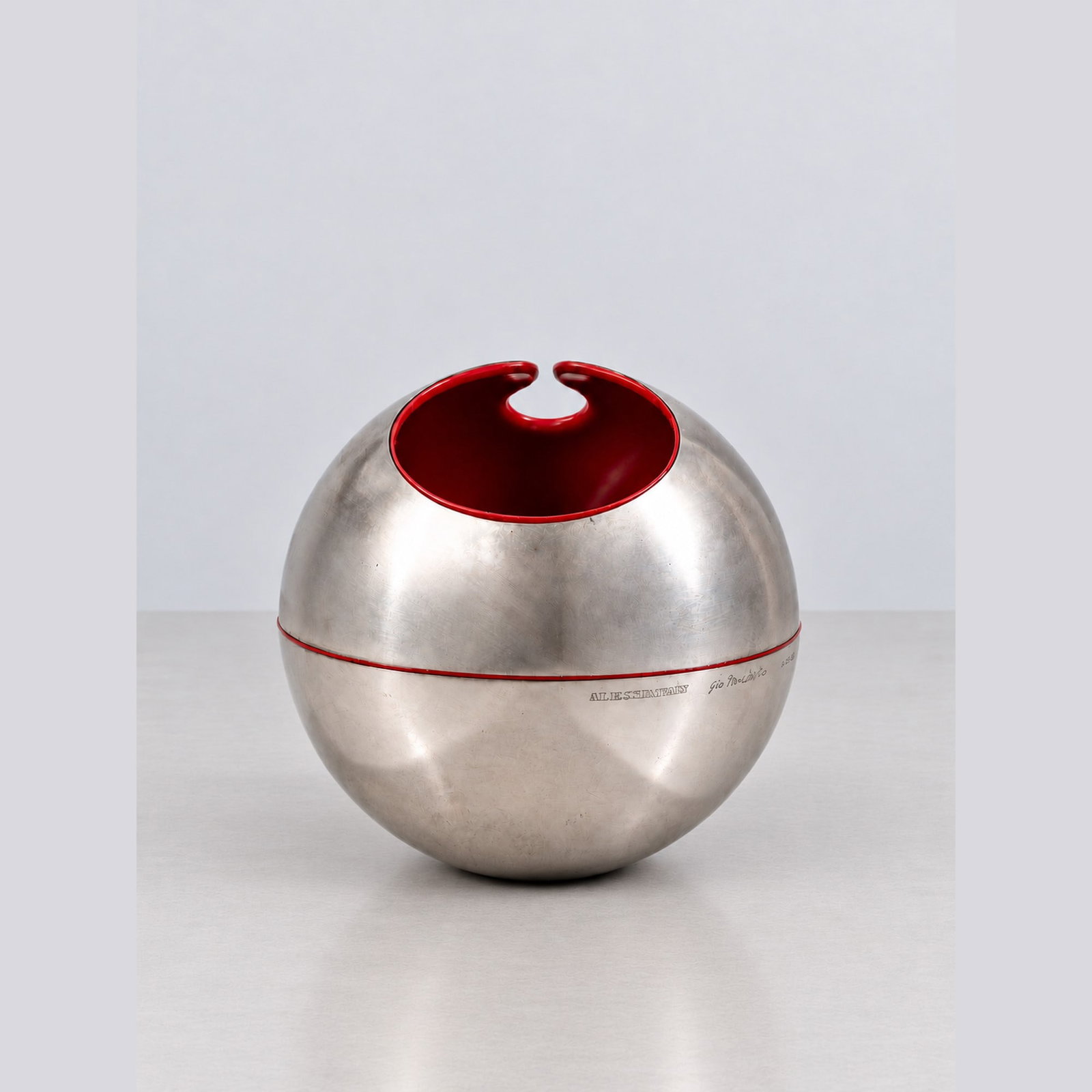 Giò Pomodoro (Orciano di Pesaro 1930 - 2002), GUSCIO N. 1, circa 1968: h cm 18 x d cm 20 Stainless steel with red polypropylene interior. Signed by Giò Pomodoro, engraved Alessi d'Après mark and serial number. Produced by Alessi d'Après, Italy.