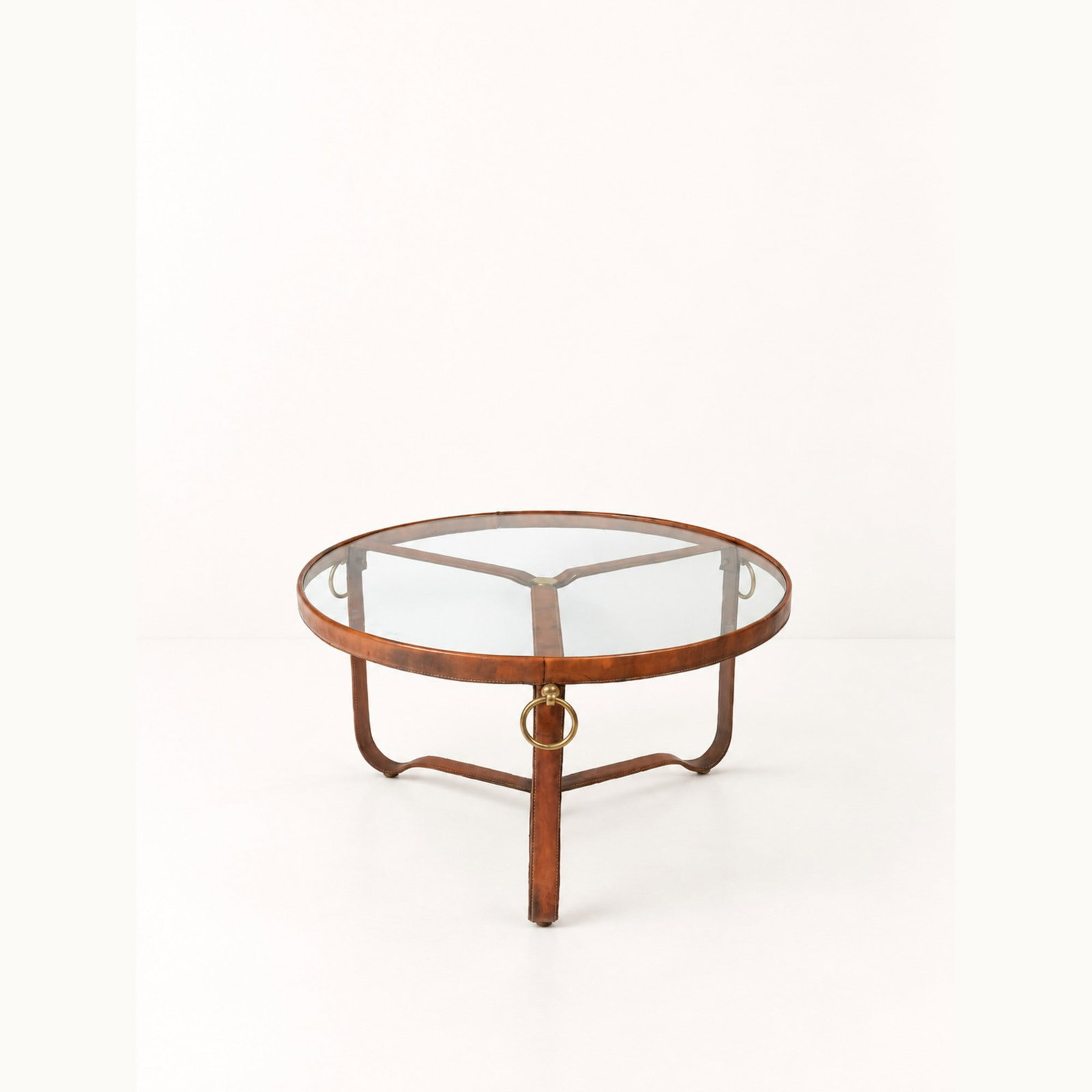 Jacques Adnet (Châtillon-Coligny 1900 - 1984), LOW TABLE, circa 1950s: h cm 45 x d cm 80 Leather-covered frame with brass fittings and glass top. French production.