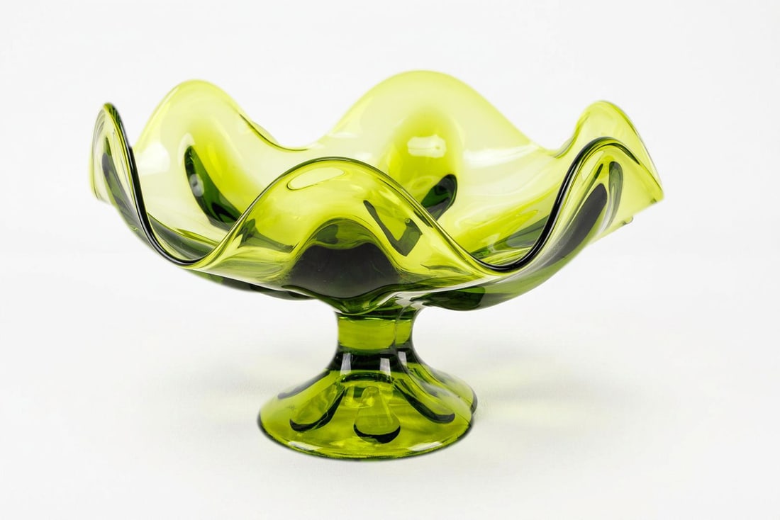 Vintage Viking Glass Pedestal Compote in Avocado Green: From the Epic line by Viking Glass, this pedestal compote bowl is crafted in sleek avocado green glass to add a pop of color to the living space. Petal motifs along its base and a wavy edge design