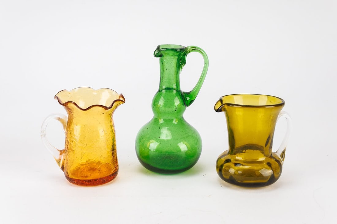 Mid Century Earth Tone Glass Trio: Includes a brown crackle glass pitcher with a ruffled edge, an avocado green pitcher with a fluted opening, and a bulbous green pitcher with a single handle.?