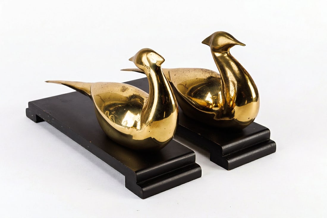 Pair of Vintage Pheasant Statues: Two brass tone bird statues mounted on a wood base. Surface of the bird has a patina of dark spots in some areas, one of them has a dent. The bases have some nicks and chips along the edge.