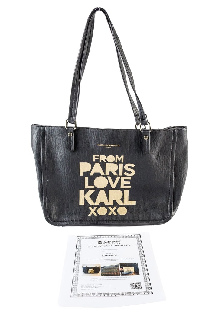 Karl Lagerfeld Paris Tote Bag: Karl Lagerfeld black tote bag with “From Paris Love Karl XOXO” printed on the side. One exterior pocket, and three interior pockets. There are cracks in the trim at the top edge of the bag. A