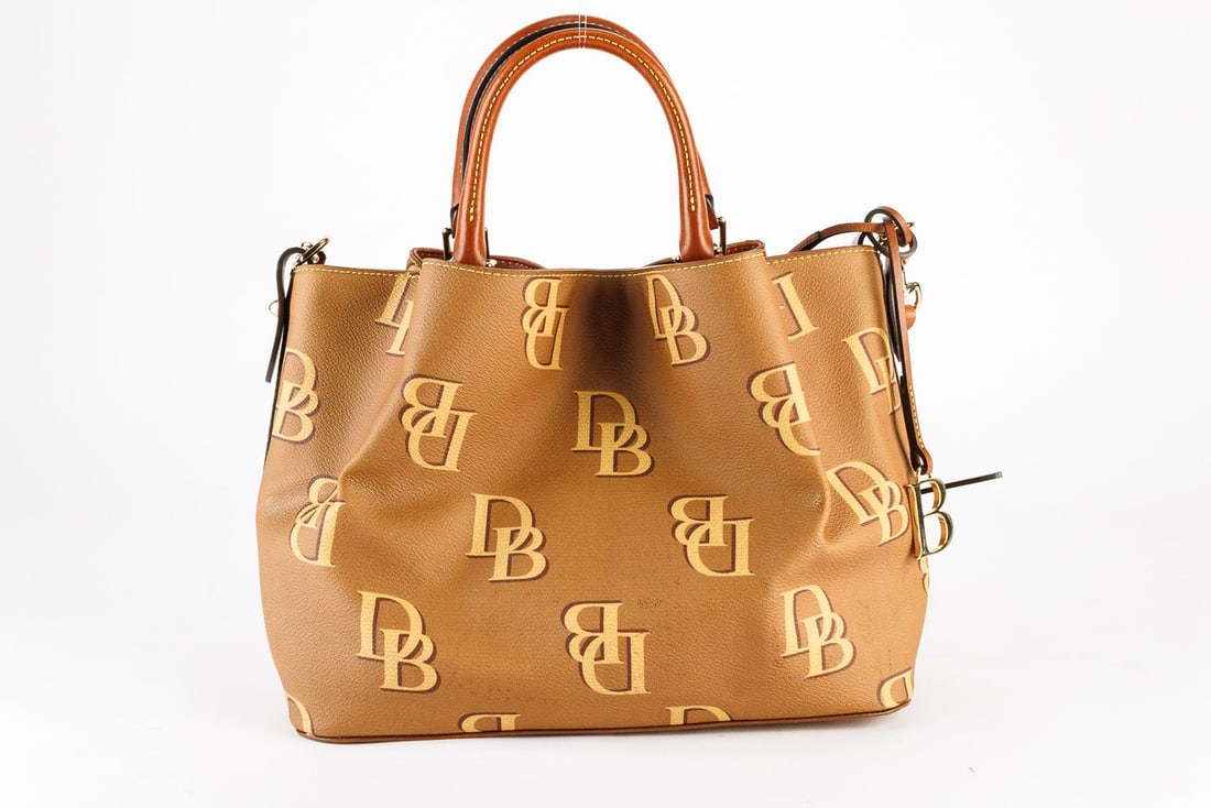 Dooney & Bourke Monogram Shoulder Bag: Dooney & Bourke monogram shoulder bag with gold tone hardware and canvas lining. There are some faint brown marks on the side of the purse. A faint cigarette smell is present.