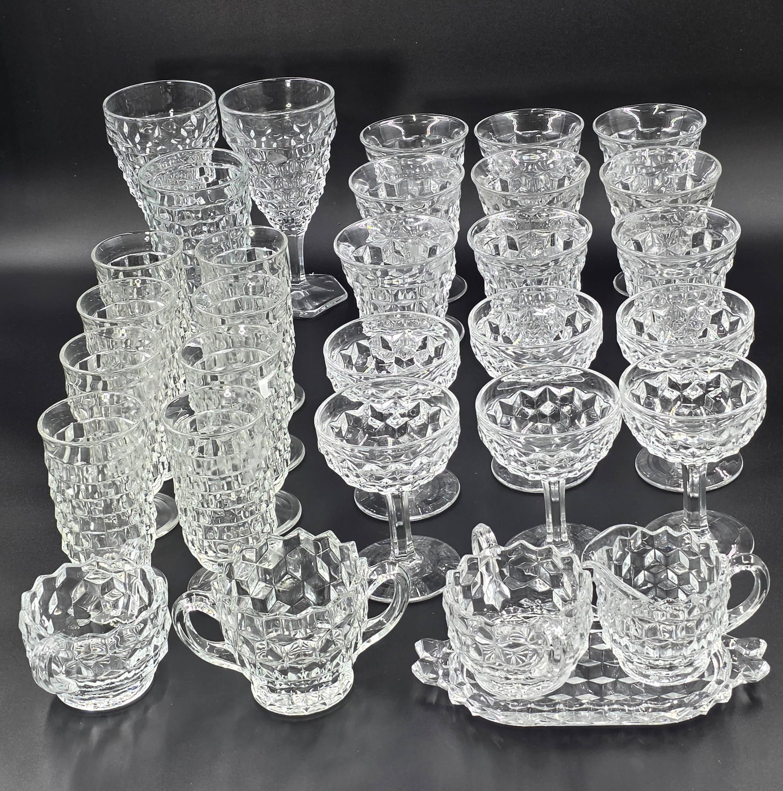 31 Fostoria American Clear Cube Motif Glassware, INV. 1049: Including water goblets, low water goblets, juice glasses, champagne tall sherbert, sugar bowls, creamers, tray, tumbler. 6 37/8" height of tallest water goblet. 4 5/8" height of sherbert.