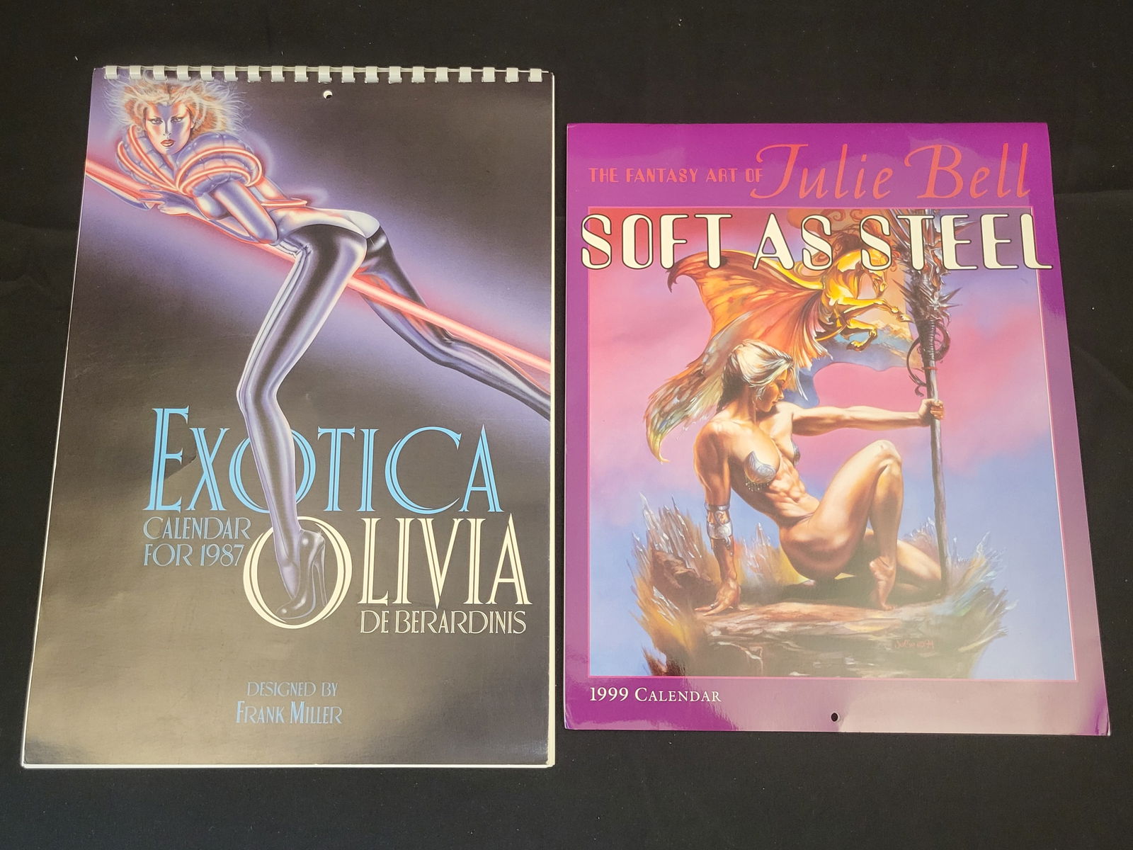Two Fantasy Art Calendars Including Olivia De Berardinis Exotica 1987 and Julie Bell Soft as Steel: BID PER WHAT YOU SEE IN THE PHOTO, NOT THE AI GENERATED TITLES AND DESCRIPTIONS! This lot features two oversized wall calendars focused on fantasy and pin-up art. The first is the Exotica calendar for