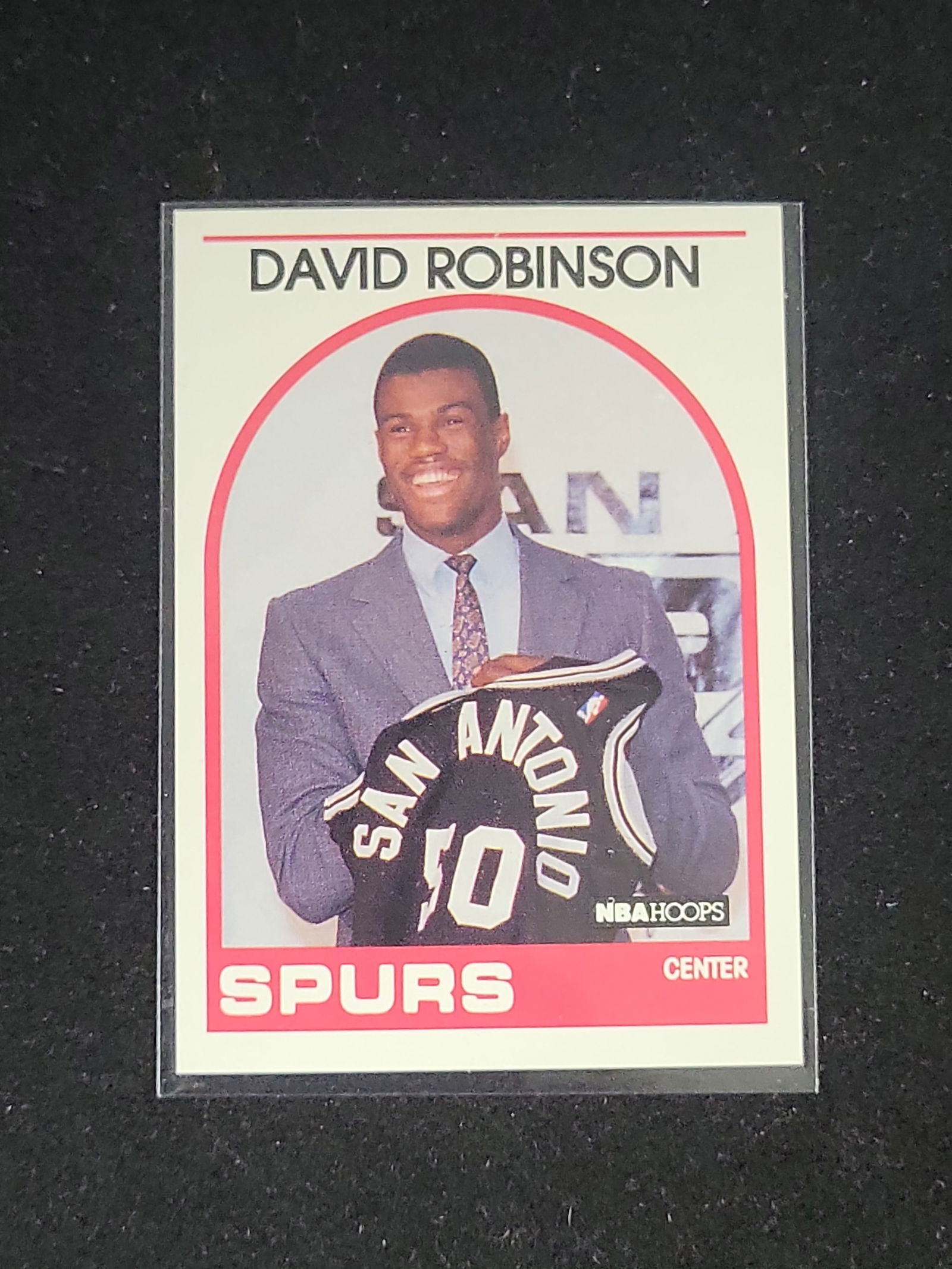 I01098 | 1989-90 NBA Hoops David Robinson Rookie Card #138: BID PER WHAT YOU SEE IN THE PHOTO, NOT THE AI GENERATED TITLES AND DESCRIPTIONS! 1989-90 NBA Hoops David Robinson Rookie Card #138This is a 1989-90 NBA Hoops David Robinson rookie card, number 138. A