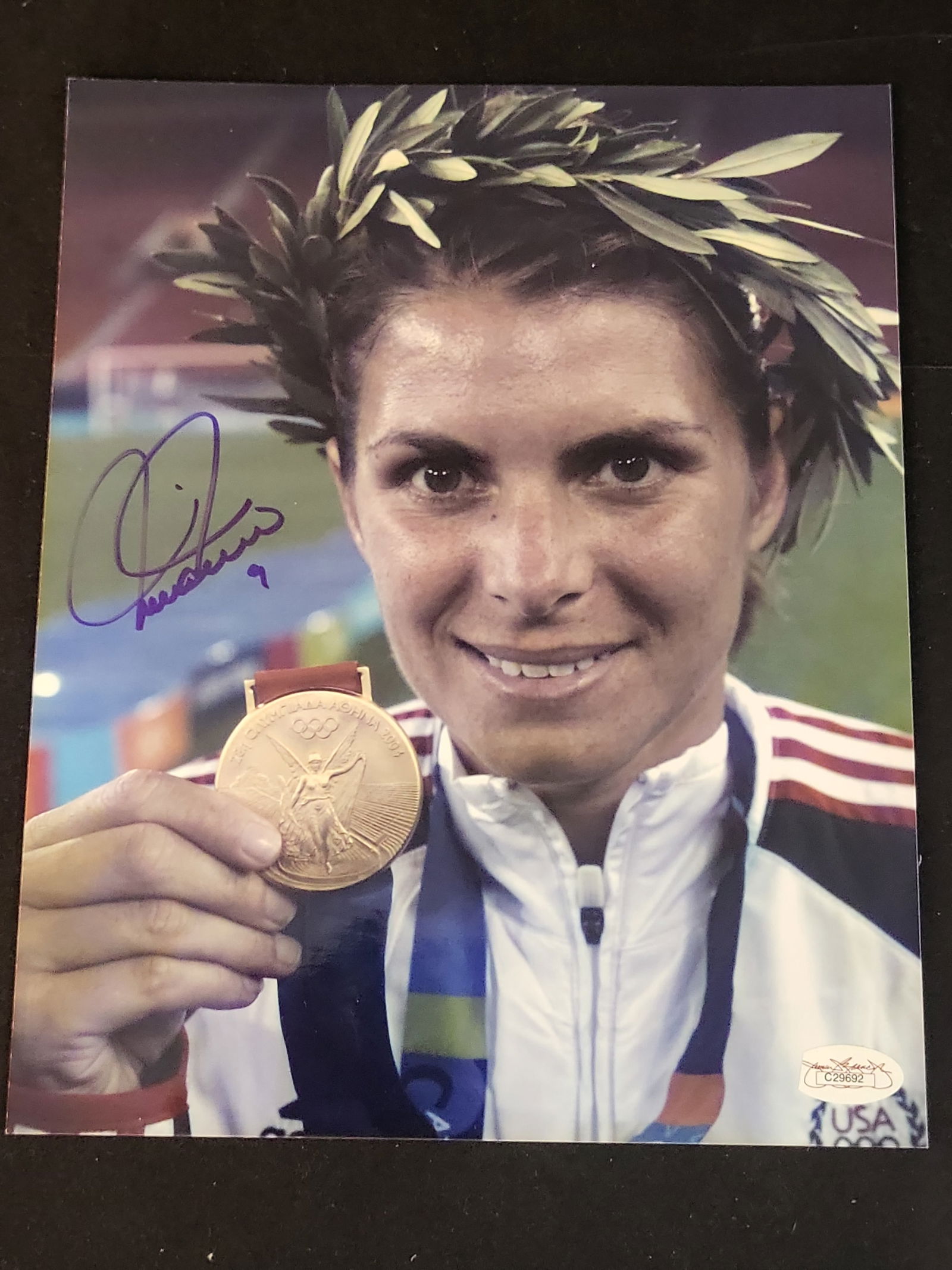I00961 | Mia Hamm Signed 2004 Olympic Gold Medal Photograph, JSA Authenticated: BID PER WHAT YOU SEE IN THE PHOTO, NOT THE AI GENERATED TITLES AND DESCRIPTIONS! Mia Hamm Signed 2004 Olympic Gold Medal Photograph, JSA AuthenticatedThis professional color photograph features Americ
