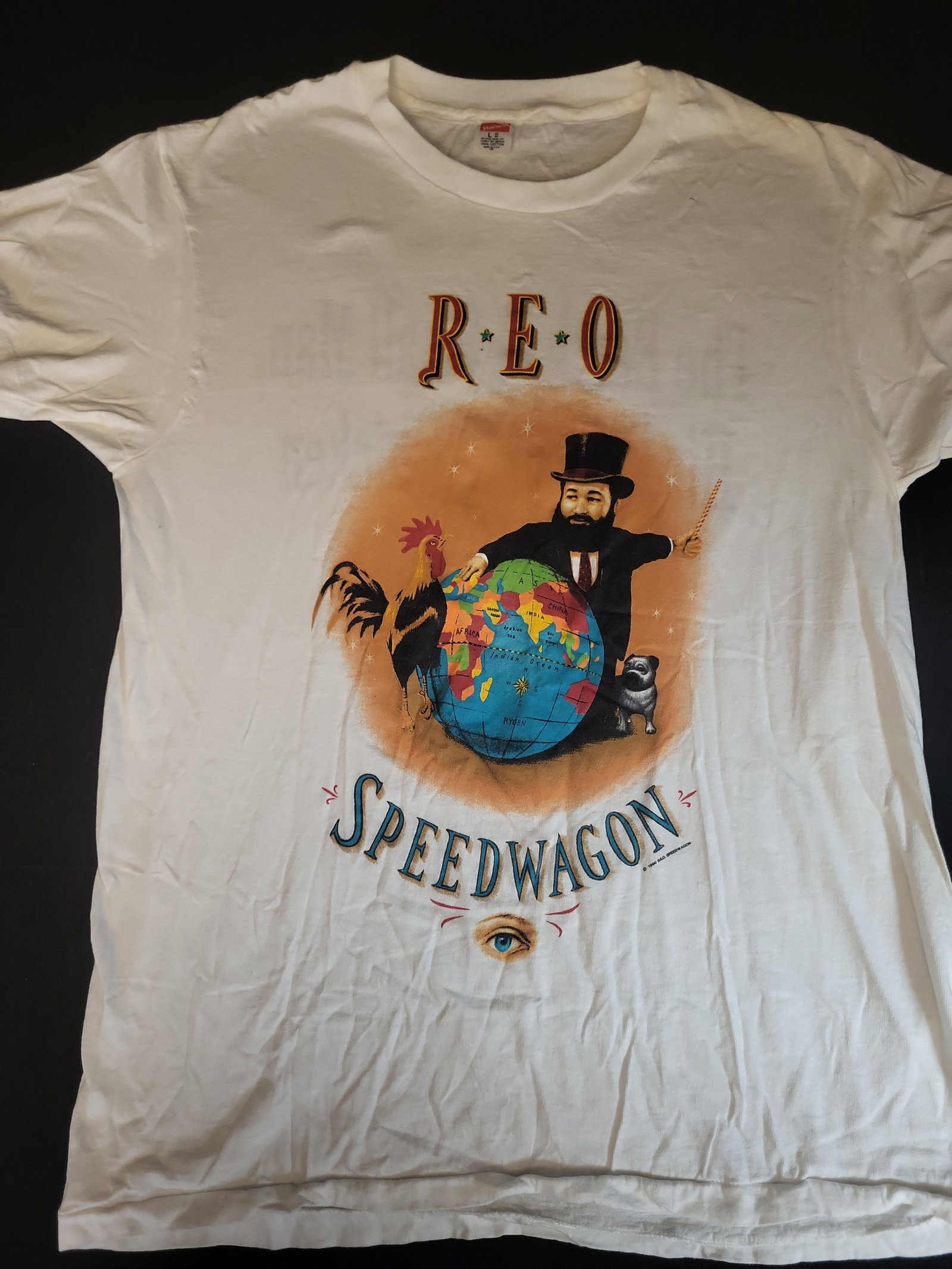 I02755 | Vintage 1990 REO Speedwagon The Earth A Small Man His Dog and a Chicken T-Shirt: BID PER WHAT YOU SEE IN THE PHOTO, NOT THE AI GENERATED TITLES AND DESCRIPTIONS! Vintage 1990 REO Speedwagon The Earth A Small Man His Dog and a Chicken T-Shirt This vintage white short-sleeve crew ne