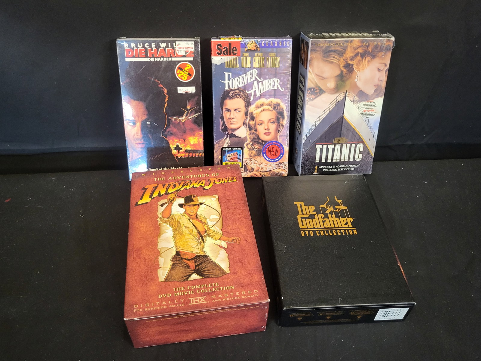 I00158 | A Collection of VHS and DVD Movie Titles including The Adventures of Indiana Jones and The: BID PER WHAT YOU SEE IN THE PHOTO, NOT THE AI GENERATED TITLES AND DESCRIPTIONS! A collection of cinematic titles in VHS and DVD formats. The group features The Adventures of Indiana Jones: The Comple