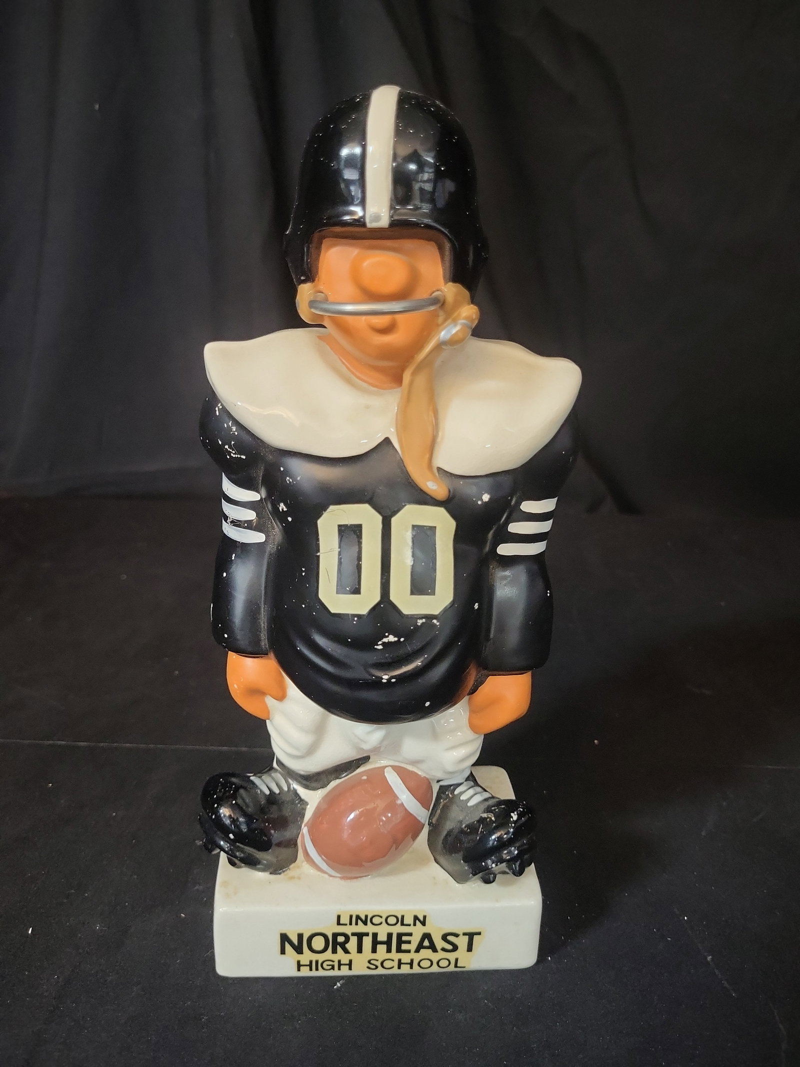 I03258 | Vintage Lincoln Northeast High School Ceramic Football Player Promotional Coin Bank: BID PER WHAT YOU SEE IN THE PHOTO, NOT THE AI GENERATED TITLES AND DESCRIPTIONS! A vintage ceramic promotional coin bank depicting a stylized football player, attributed to designer Fred Kail. The fig