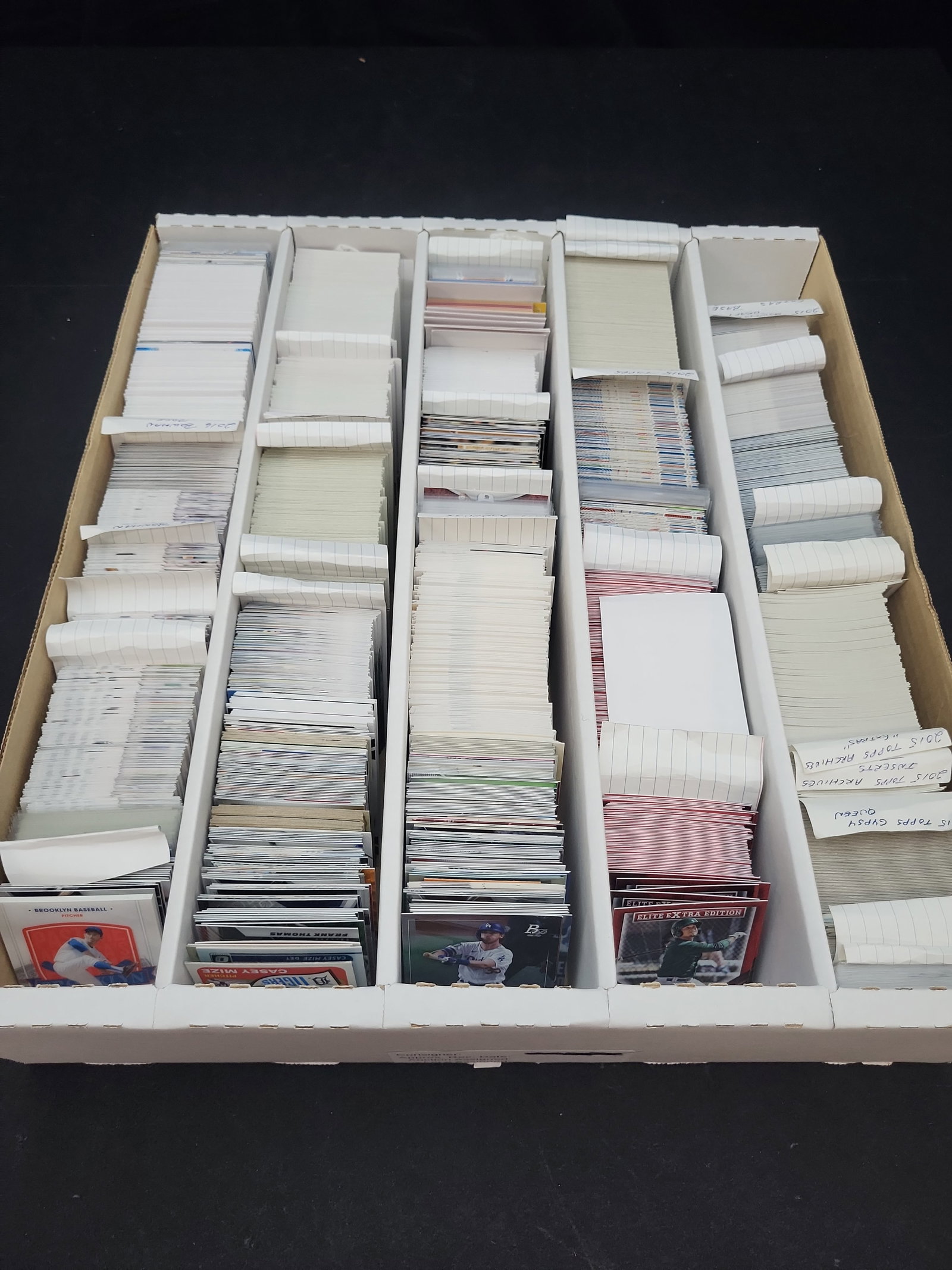 I03322 | An Assortment of Modern Baseball Trading Cards Featuring Topps, Bowman, and Panini, circa: BID PER WHAT YOU SEE IN THE PHOTO, NOT THE AI GENERATED TITLES AND DESCRIPTIONS! A large collection of baseball trading cards organized in a multi-row cardboard storage box. The collection is sorted w