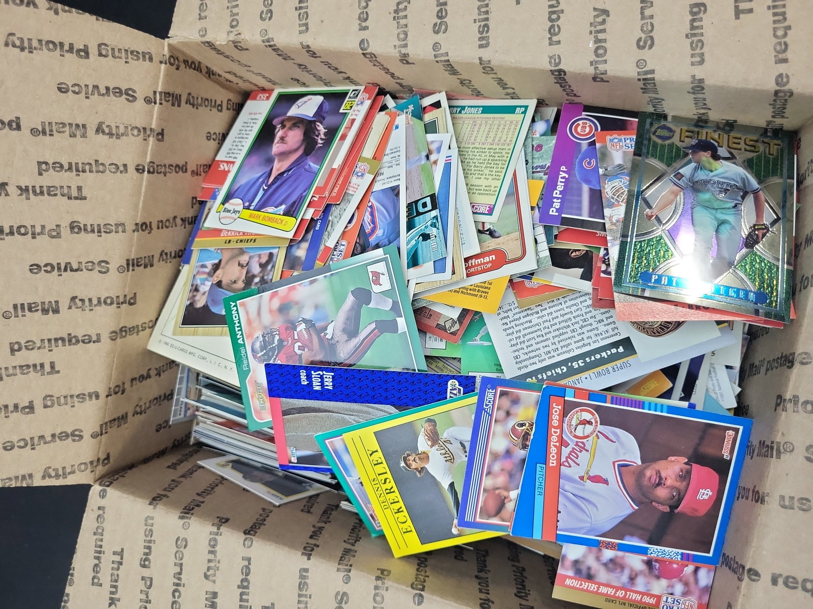 I03329 | An Assortment of Vintage Sports Trading Cards Including Baseball, Football, and Basketball,: BID PER WHAT YOU SEE IN THE PHOTO, NOT THE AI GENERATED TITLES AND DESCRIPTIONS! An assortment of ungraded, loose sports trading cards spanning the late 1970s through the mid-1990s. This bulk lot feat