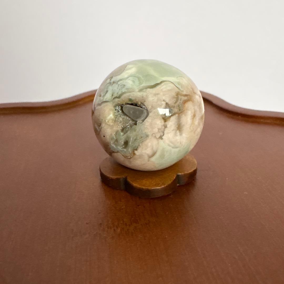 Green Cherry Blossom Agate: Green Cherry Blossom Agate, 28.5 mm, with Wooden Base. This is a rare collectible: a piece of green cherry blossom agate geode filled with small pebbles. The geode is covered by these pebbles, but in