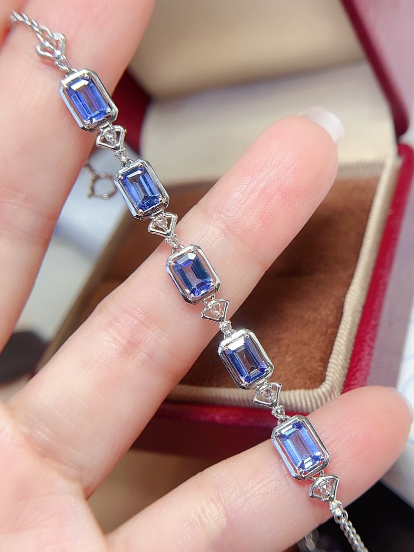 18K Gold Flawless Tanzanite Bracelet: This bracelet is crafted in 18K gold, featuring a flawless glassy tanzanite that exudes elegance. The emerald-cut main stone captivates at first sight, complemented by 12 white sapphires that add bril