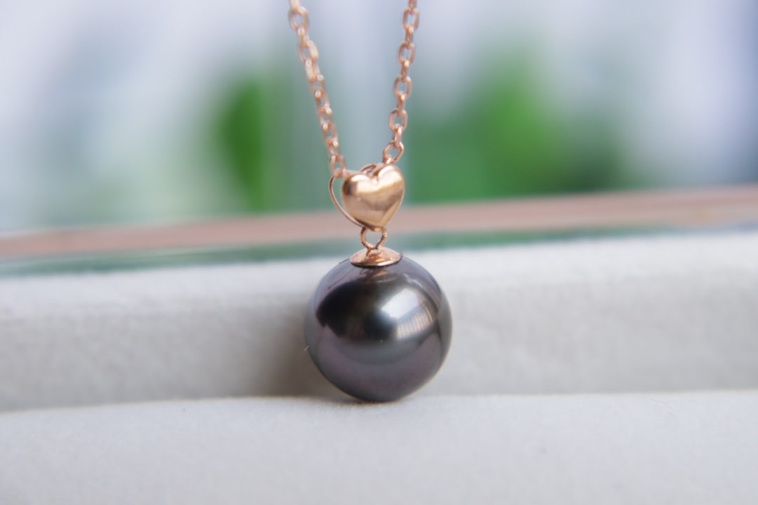 18K Gold Tahitian Pearl Pendant: This pendant is crafted from 18K gold and features a Tahitian pearl with a diameter of 9.4mm. The pearl is perfectly round with a strong luster and a captivating iridescence, despite minor blemishes