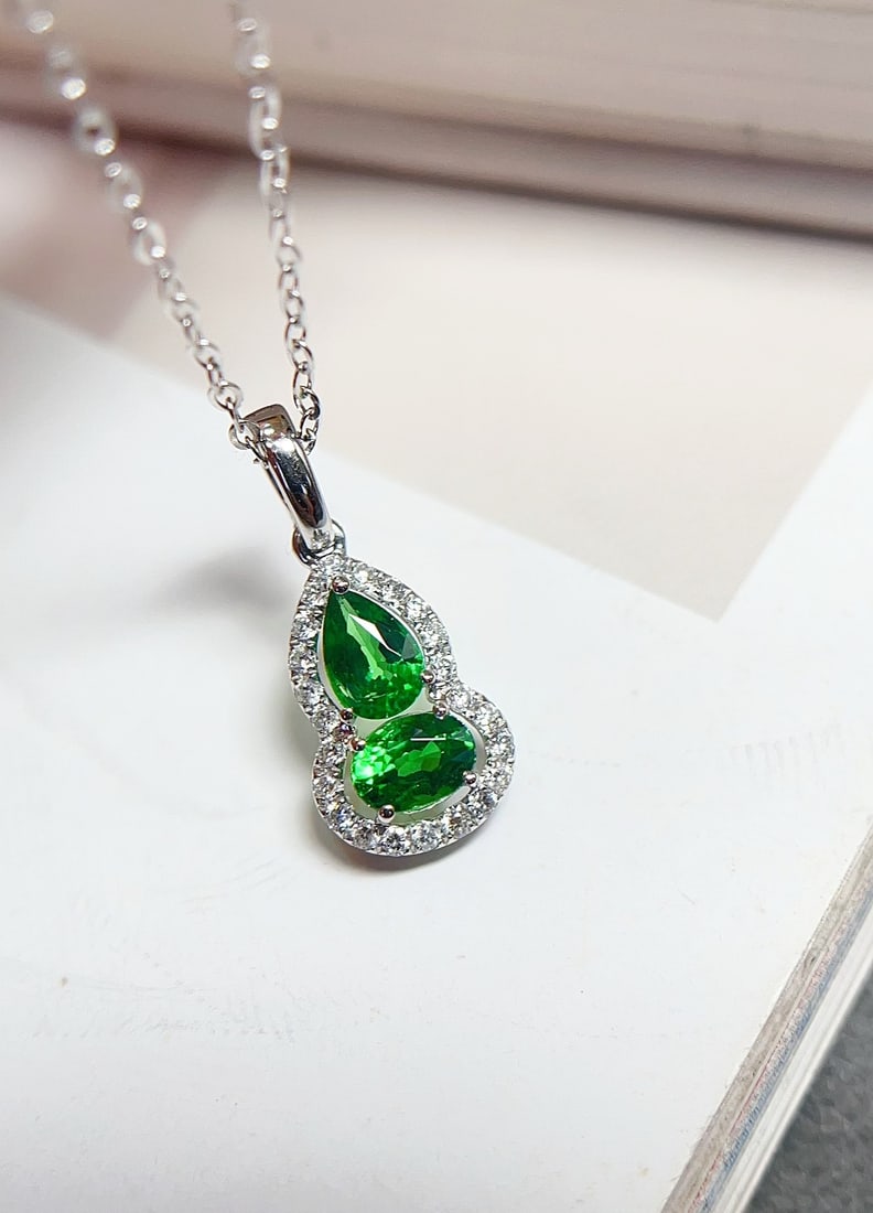 18K Gold Tsavorite Pendant: This pendant is meticulously crafted in 18K gold, featuring a unique gourd design that exudes a sense of fashion and freshness. The vivid green hue of the main stone complements the glassy texture bea