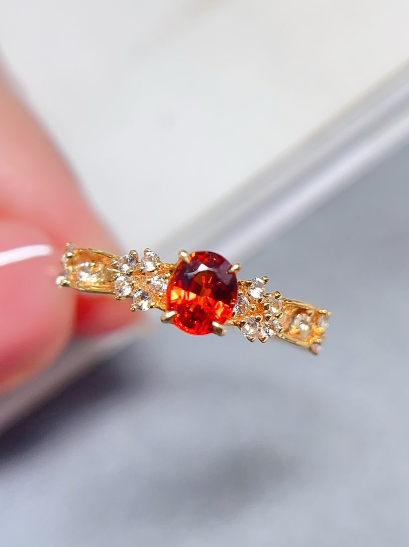 18K Gold Fanta Ring: This ring, centered around a vibrant orange Fanta gemstone, exudes a bold and unique beauty, shimmering brilliantly in the light. Adorned with 16 white and blue sapphires, the overall design is sophis