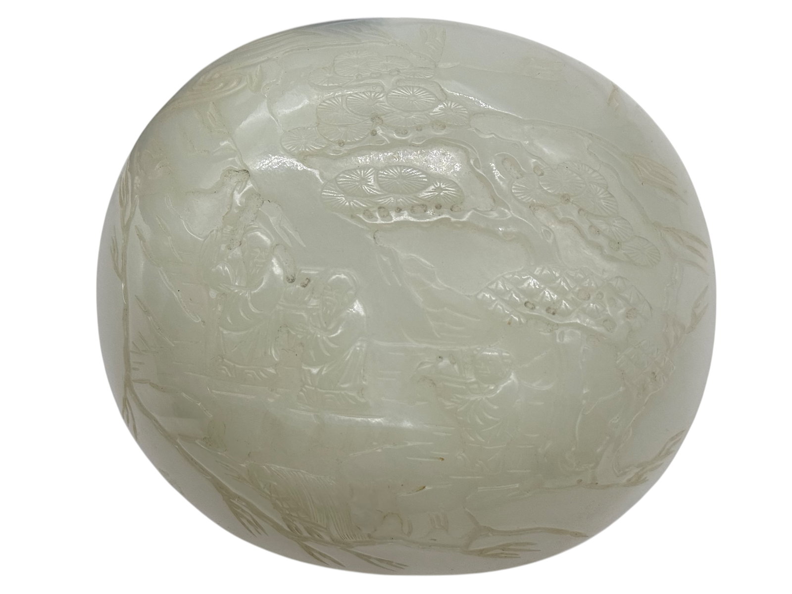 A Carved White Jade Cover: Of domed form, finely carved in shallow relief with scholars and attendants in a pine landscape, the stone of a pale celadon-white tone with natural inclusions. L: 14inchesW? 12 1/2 inchesH: 1 inches