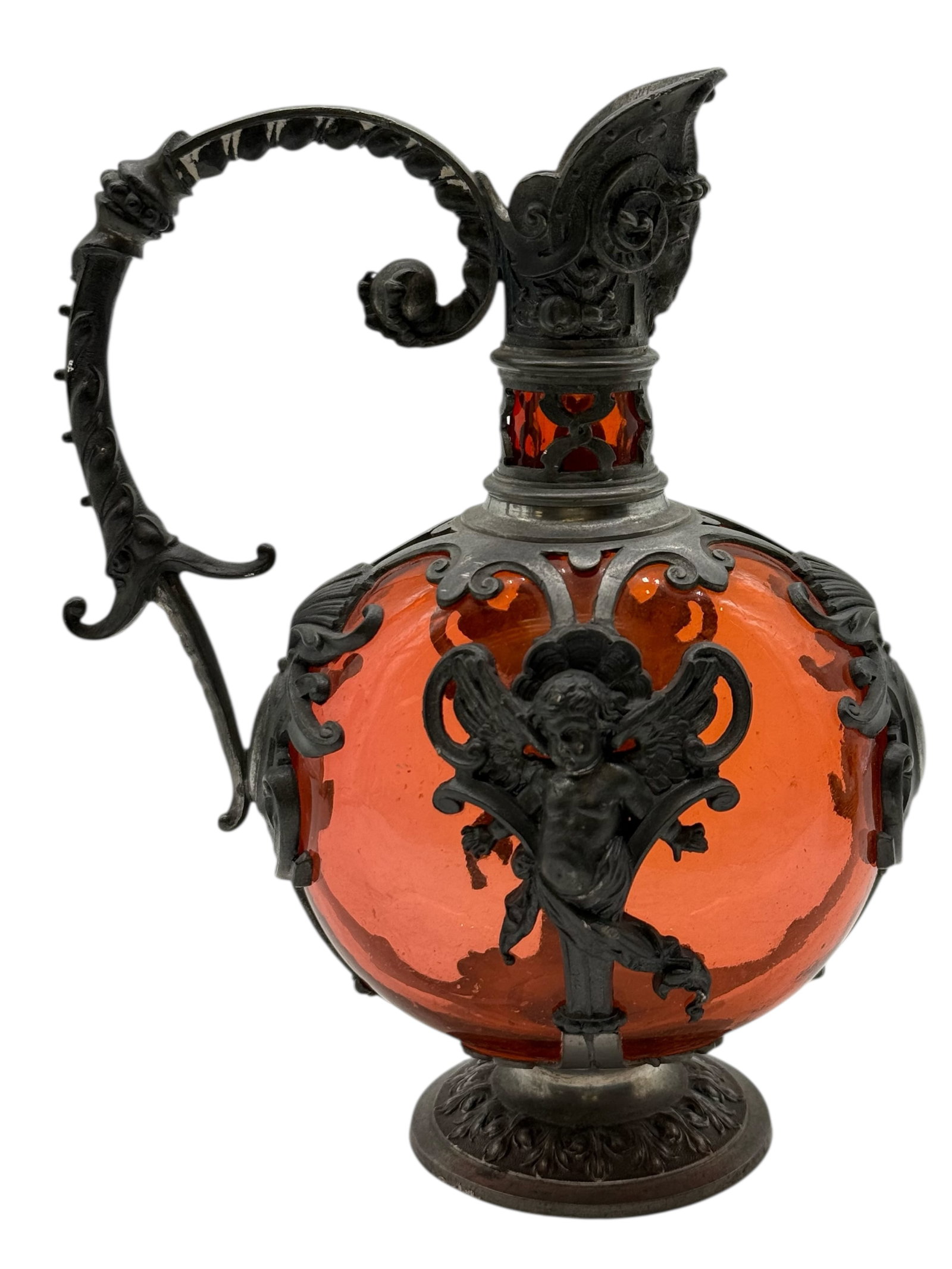 A Continental Glass Ewer with Metal Mounts Pewter: The spherical amber-colored glass body applied with scrolling metal mounts and a winged cherub mask, fitted with a shaped spout, scrolling handle H: 7 1/4 inches W: 6 inchesD: 3 1/4 inches