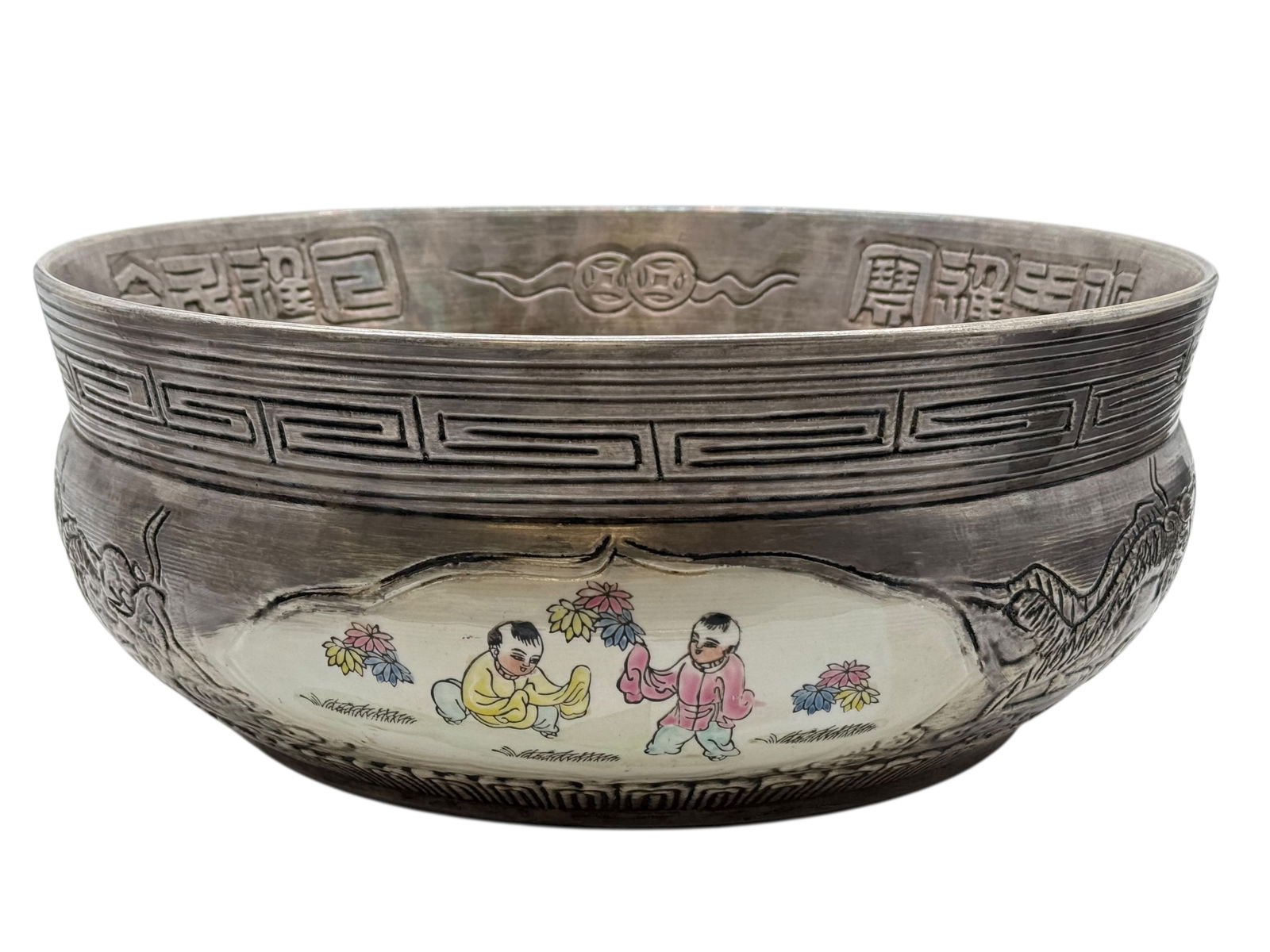 A Large Chinese Silver-Overlay Porcelain Bowl: The rounded bowl encircled with repoussé silver mounts, the porcelain body painted with boys at play among flowering plants, the interior rim with incised characters. H: 6 1/2 inchesD: 15 5/8