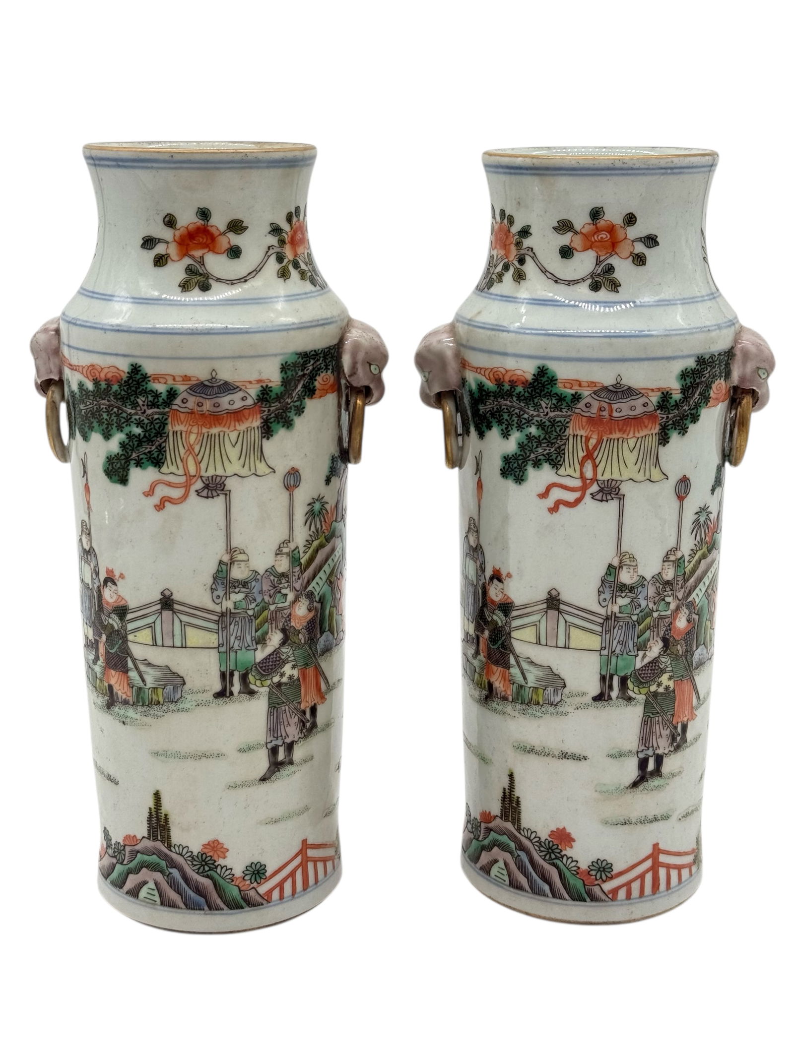 A Pair of Chinese WUCAI Figural Vases: Each of cylindrical form, painted in polychrome enamels with figural scenes in a landscape setting, the shoulders applied with lion-mask handles suspending rings; the rims with double-line