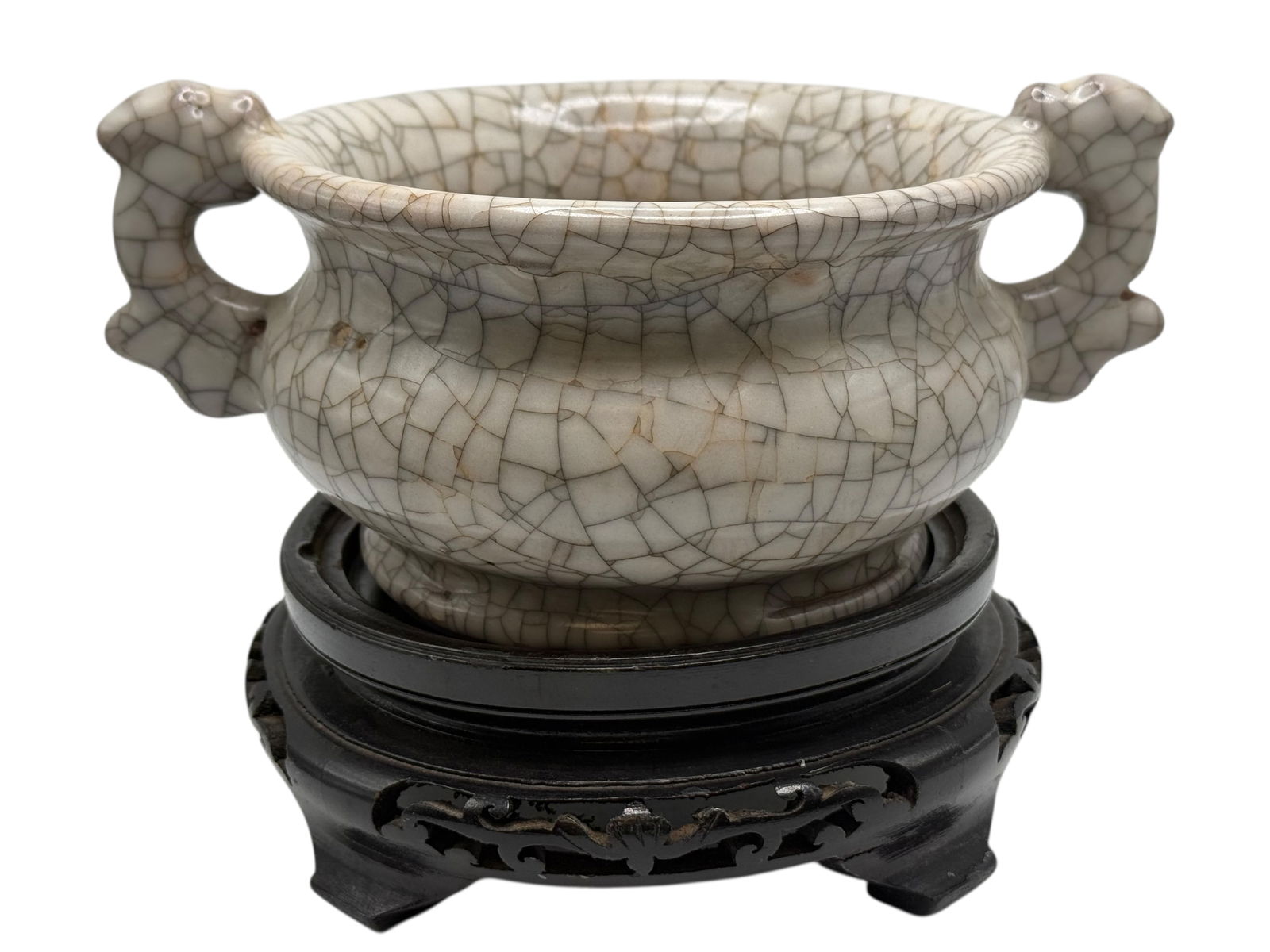 A Chinese Crackle-Glazed Two-Handled Censer: Of compressed globular form with a wide mouth, flanked by two openwork loop handles, covered overall in a pale crackle glaze, raised on a carved wooden stand. H: 3 3/4 inchesW: 8 3/4 inches