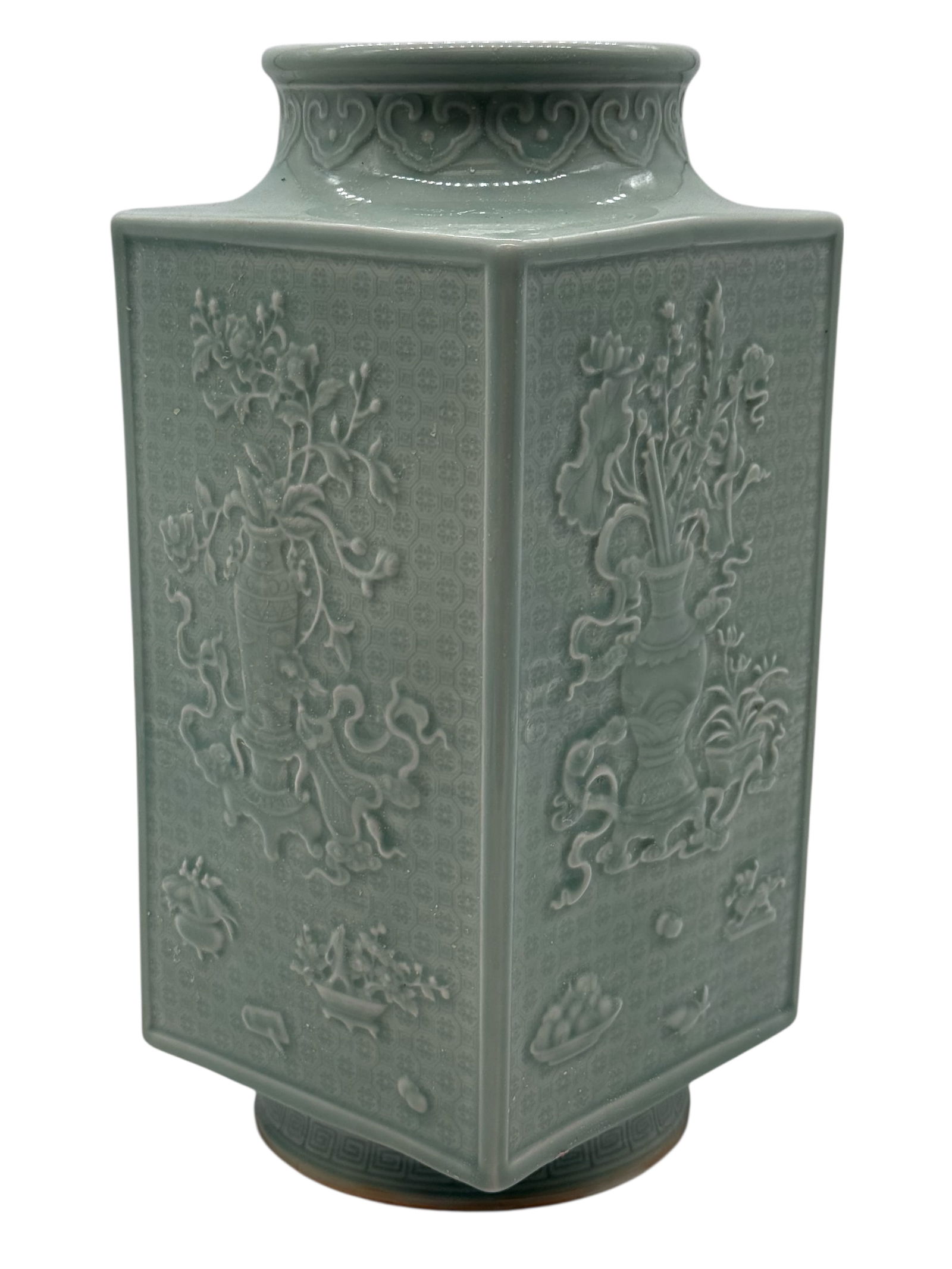 A Chinese Celadon-Glazed Diamond-Section Vase: Of diamond section with tapering sides and a short neck, each face molded in low relief with floral vases and auspicious objects against a geometric ground, covered overall with a celadon glaze.