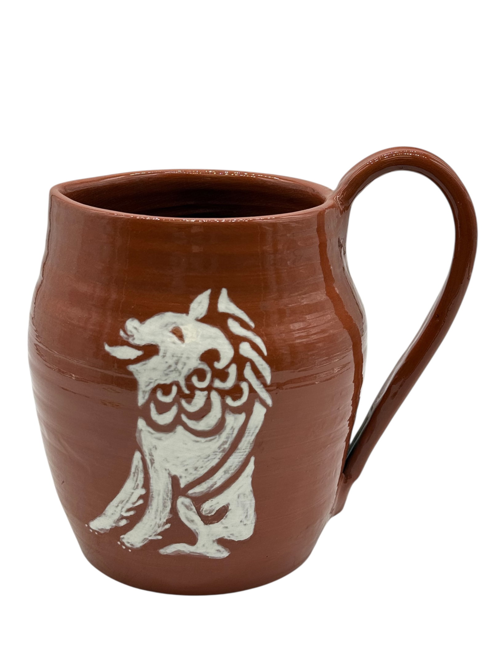 A Red Pottery Mug with Slip Decoration: Decorated with a white slip motif of a mythical beast on a red pottery body, with a loop handle. H: 8 1/4 inches W: 8 inches