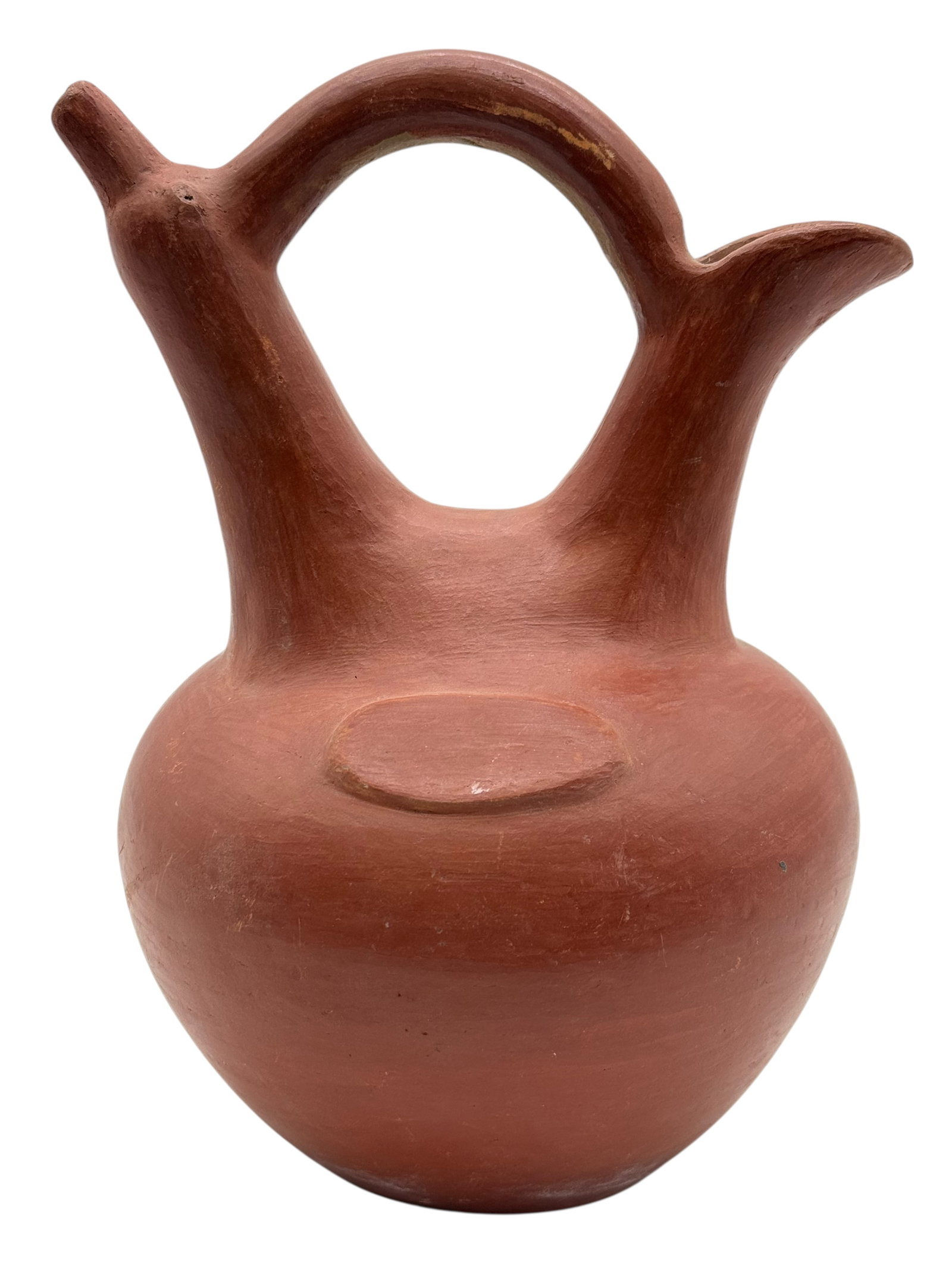 A Red Earthenware Vessel with Double Spouts: A hand-formed earthenware vessel with rounded body, loop handle, and dual opposing spouts. The surface shows uniform red slip and minor abrasions. H: 10 1/2 inchesW: 8 inches