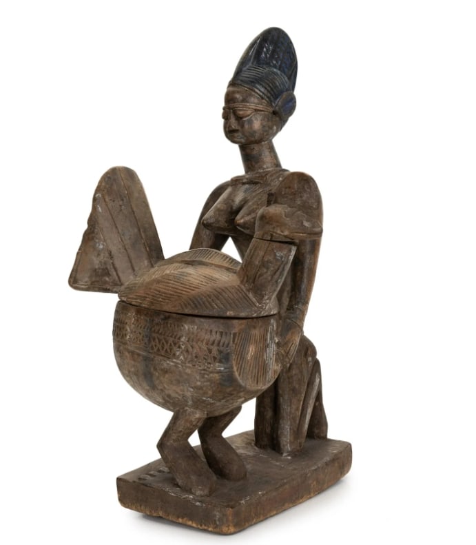 An African Carved Wood Figure with Bowl: An African Carved Wood Figure with BowlCarved as a kneeling female figure supporting a lidded bowl with geometric decoration. H:14.25in(36.1cm) W:5in(12.7cm)
