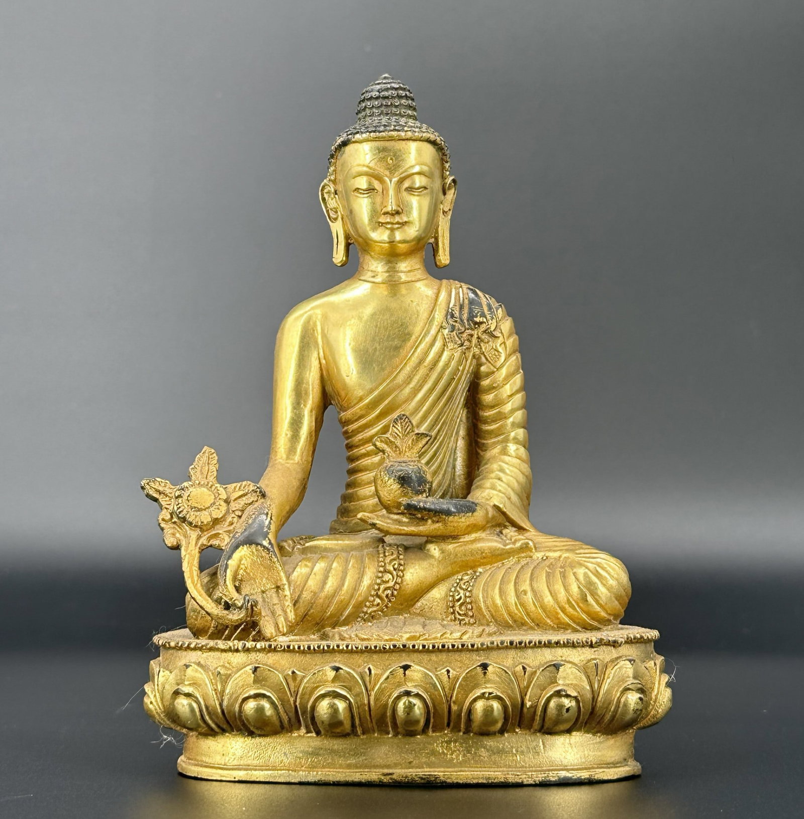 A Tibetan Gilt-Bronze Figure of Buddha: Seated in dhyanasana on a double-lotus base, holding a myrobalan fruit and branch in the hands Size: 7 1/2"H