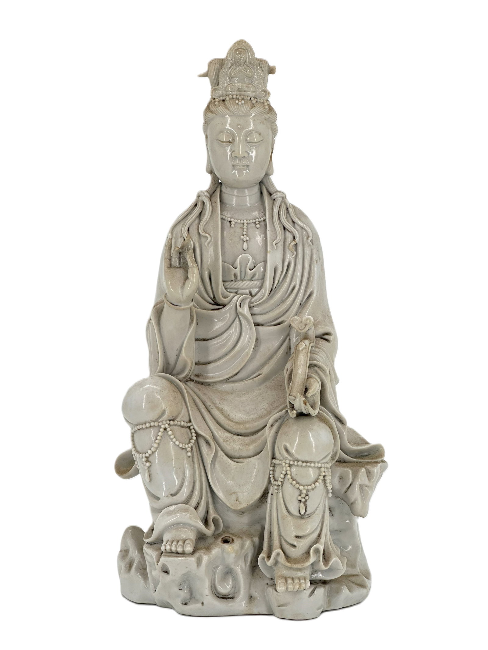 A Chinese Blanc-de-Chine Figure of Guanyin: Seated in royal ease on a rocky base, the deity holding a scroll and wearing flowing robes beneath a high cowl, covered in a cream-white glaze. Size: 11 1/2" * 5" * 4 1/2"
