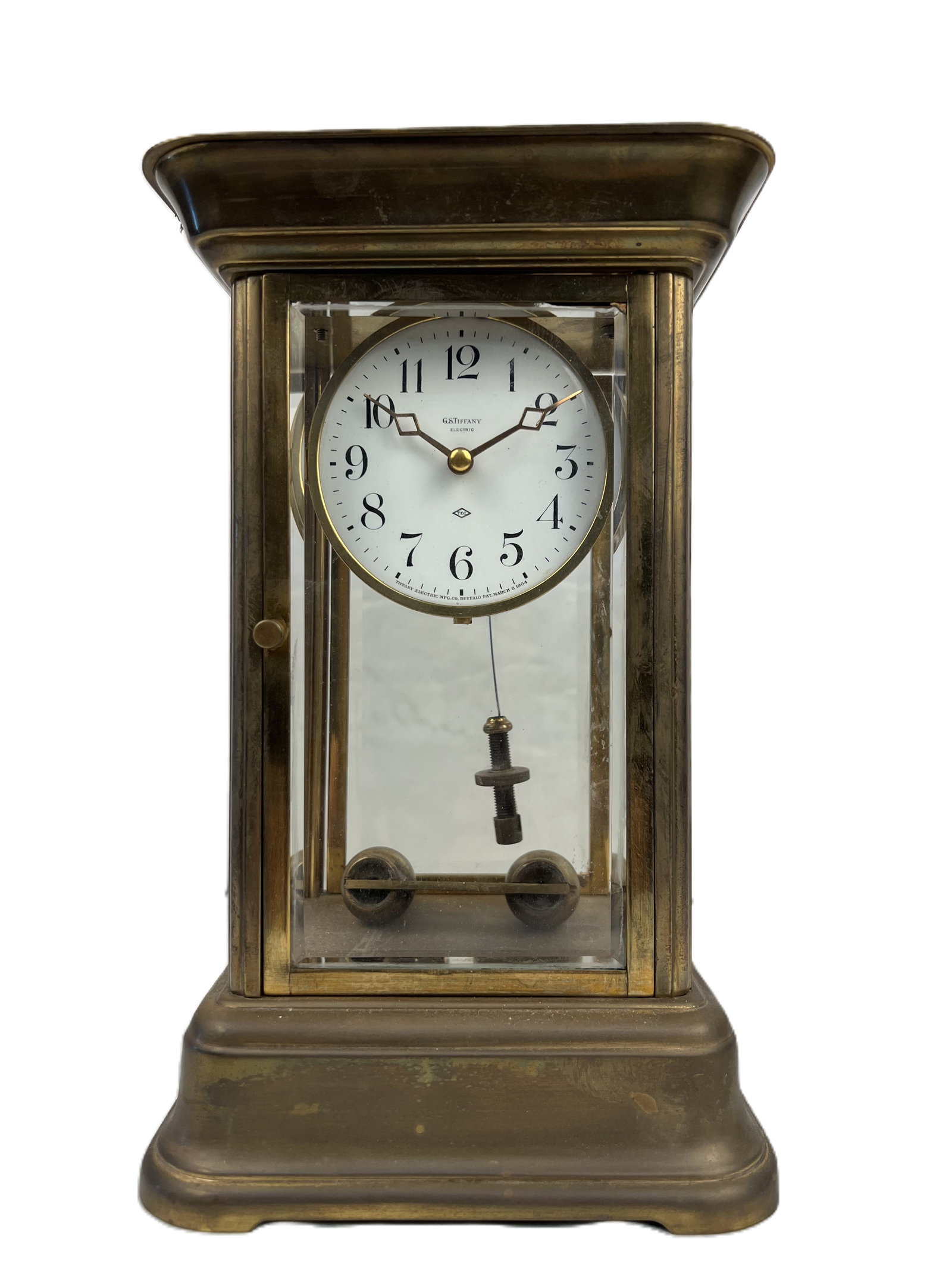 A Tiffany Electric Brass and Glass Mantel Clock: The circular dial enclosed within a glazed rectangular case with visible pendulum. Tiffany Electrical Table Clock Size: 9 1/2" * 6" * 5"