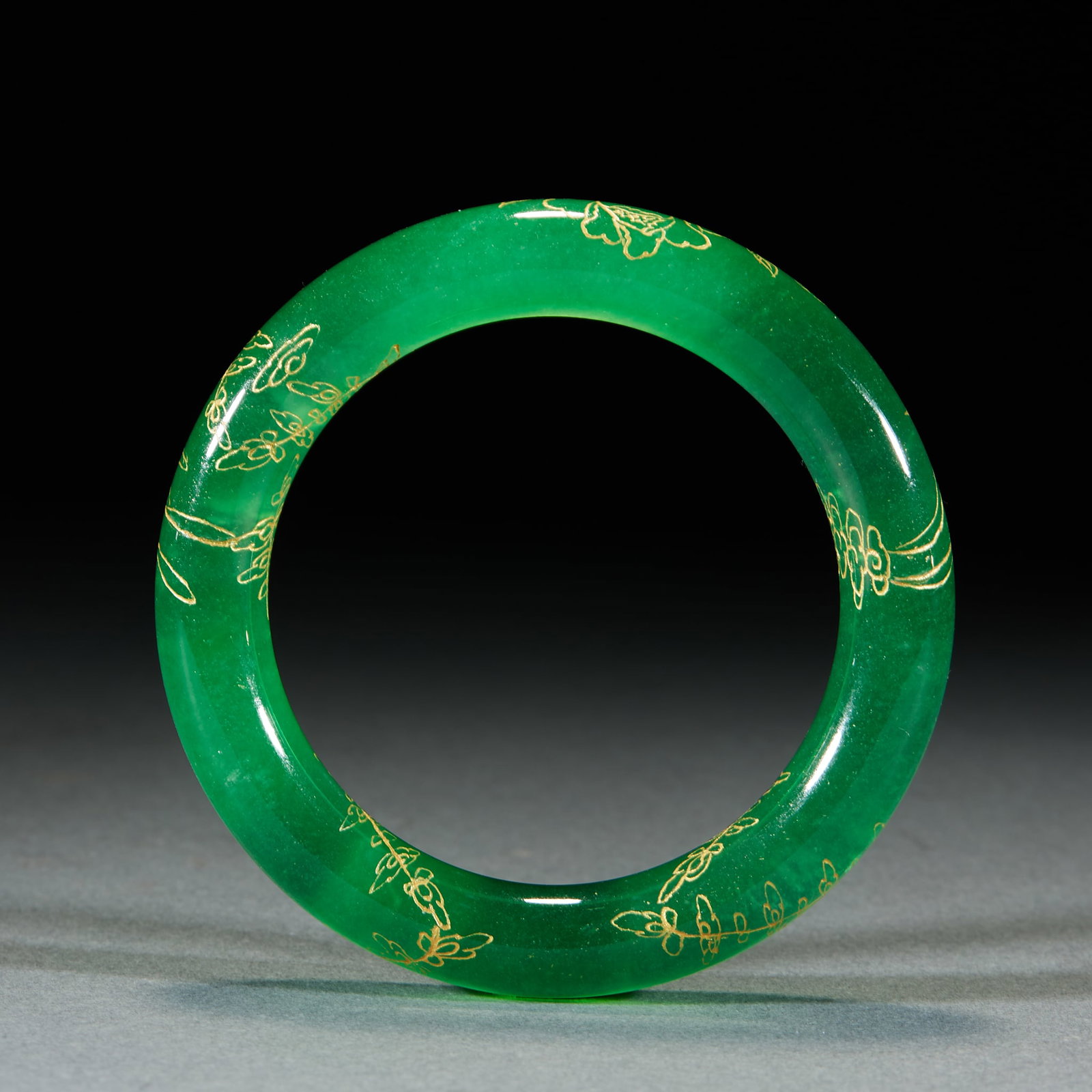 Gold Traced Jadeite Bangle: Gold Traced Jadeite Bangle: Translucent jadeite decorated with gold traced flower and cloud patterns, rich vivid emerald color and delicate traced lines. Specifications: inner diameter 6cm. Cultural v