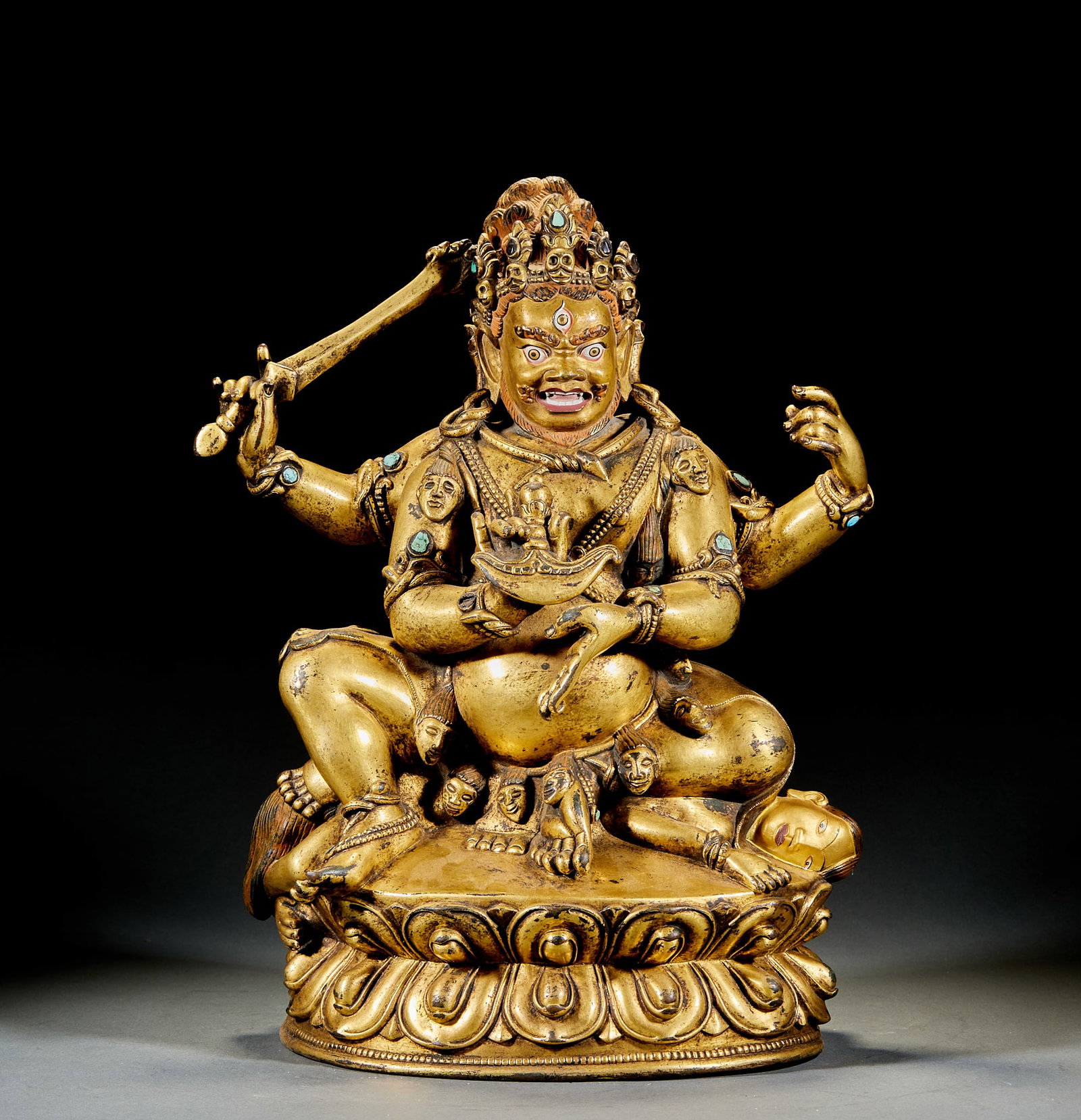 Gilt Bronze Four-Armed Mahakala: Gilt Bronze Four-Armed Mahakala Tall Statue: Majestic iconography with four arms holding ritual implements, seated on lotus base adorned with turquoise inlay accents. Height 42cm, length 32cm, width 2