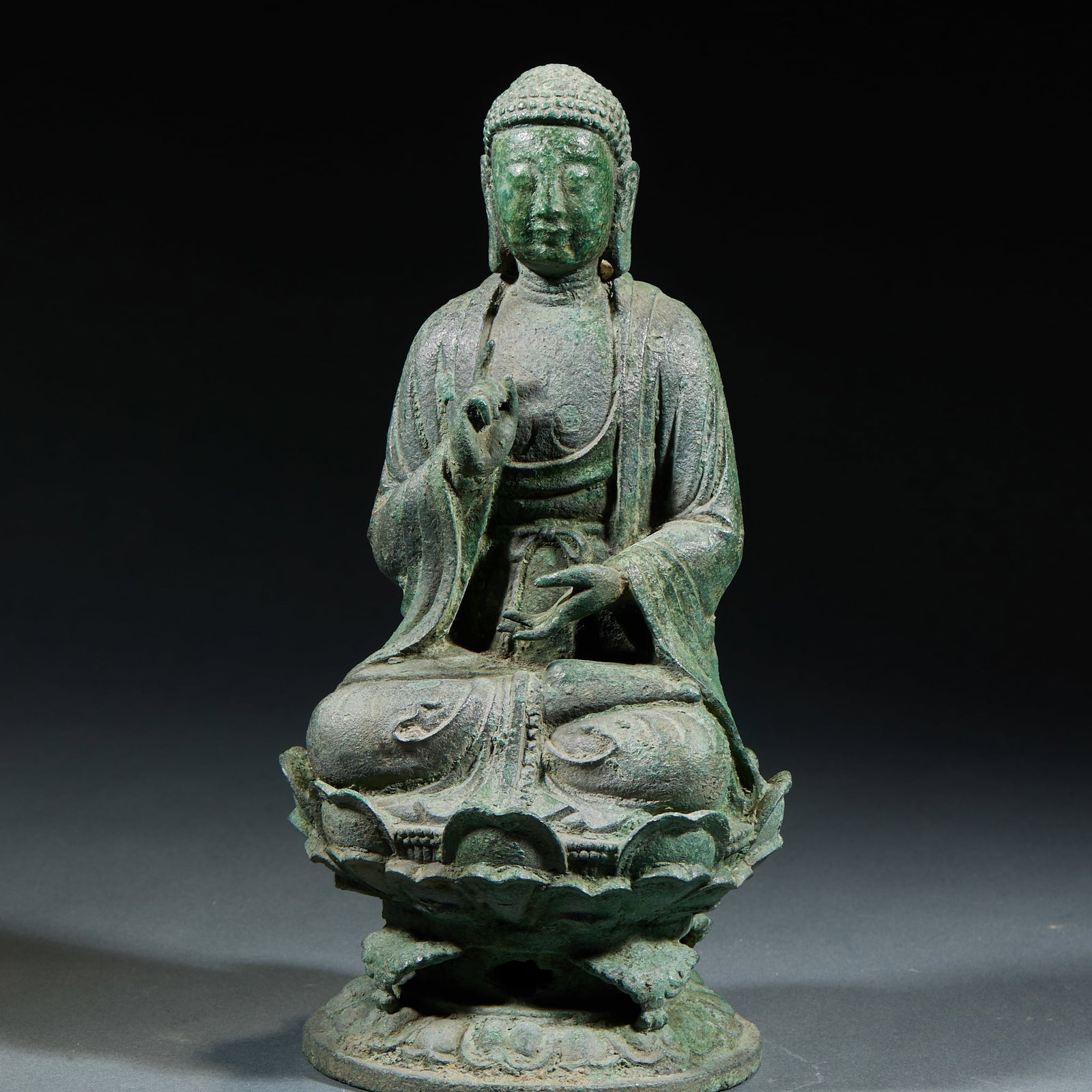 Bronze Sakyamuni Statue: Bronze Sakyamuni Seated Statue: Bronze cast Buddha seated in cross-legged posture on lotus throne, serene peaceful facial expression and concise smooth robe lines, thick natural aged patina. Height 22