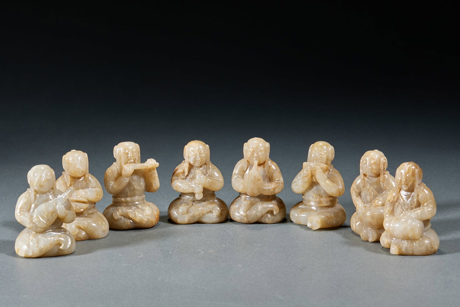 Set of Hetian Jade Khitan Figure and Musician Figurines: Set of Hetian Jade Khitan Musician Figurines, carved from ancient Hetian jade with natural patina, nine figures in total, all in cross-legged seated posture, holding various instruments including pipa