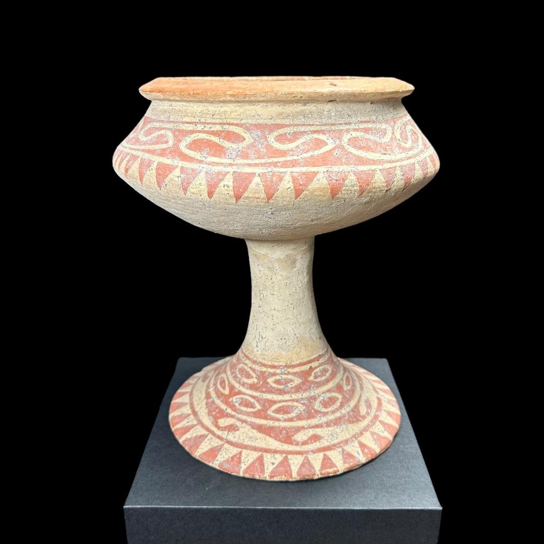 Ancient Bang Chiang footed vessel: Ancient Bang Chiang footed vessel from Thailand, ca. 300 BCE. Painted in red geometric patterns with cream ground. Four perforated holes for suspension. 9.5" H. Ex. Windsor, CT. collection, acquired p