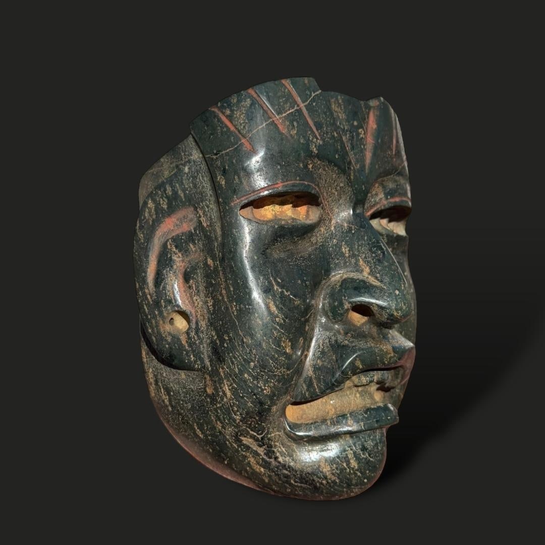 Pre-Columbian Olmec serpentine stone mask: Pre-Columbian Olmec Serpentine Mask: This striking mask, crafted from deep green serpentine stone with natural variations and weathered patina, represents the remarkable artistry of the Olmec civiliza