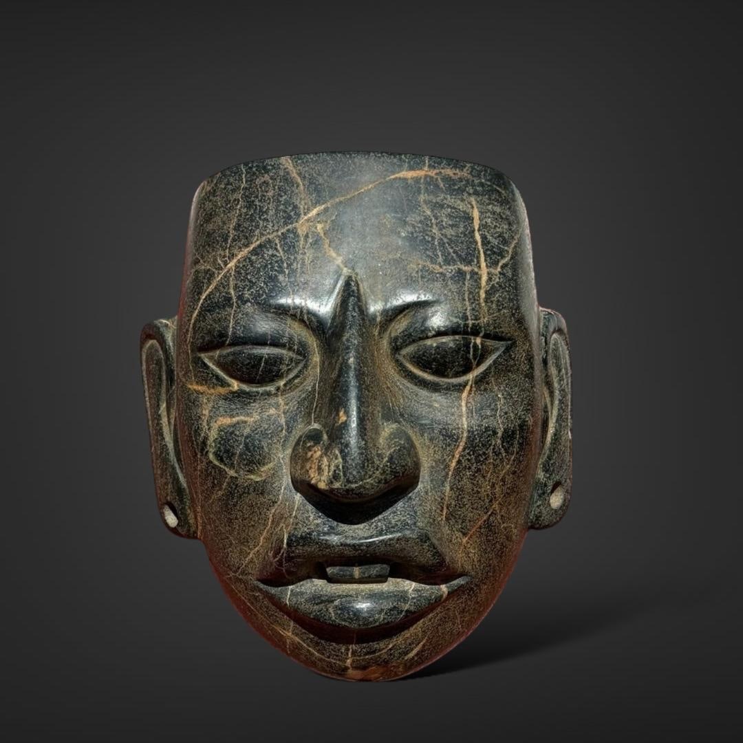 Pre-Columbian Maya stone mask: Mexico, circa 600-900 AD. Maya mask carved from dark green stone, possibly jade or a similar material. The mask features a highly detailed and realistic human face with distinct Maya characteristics.